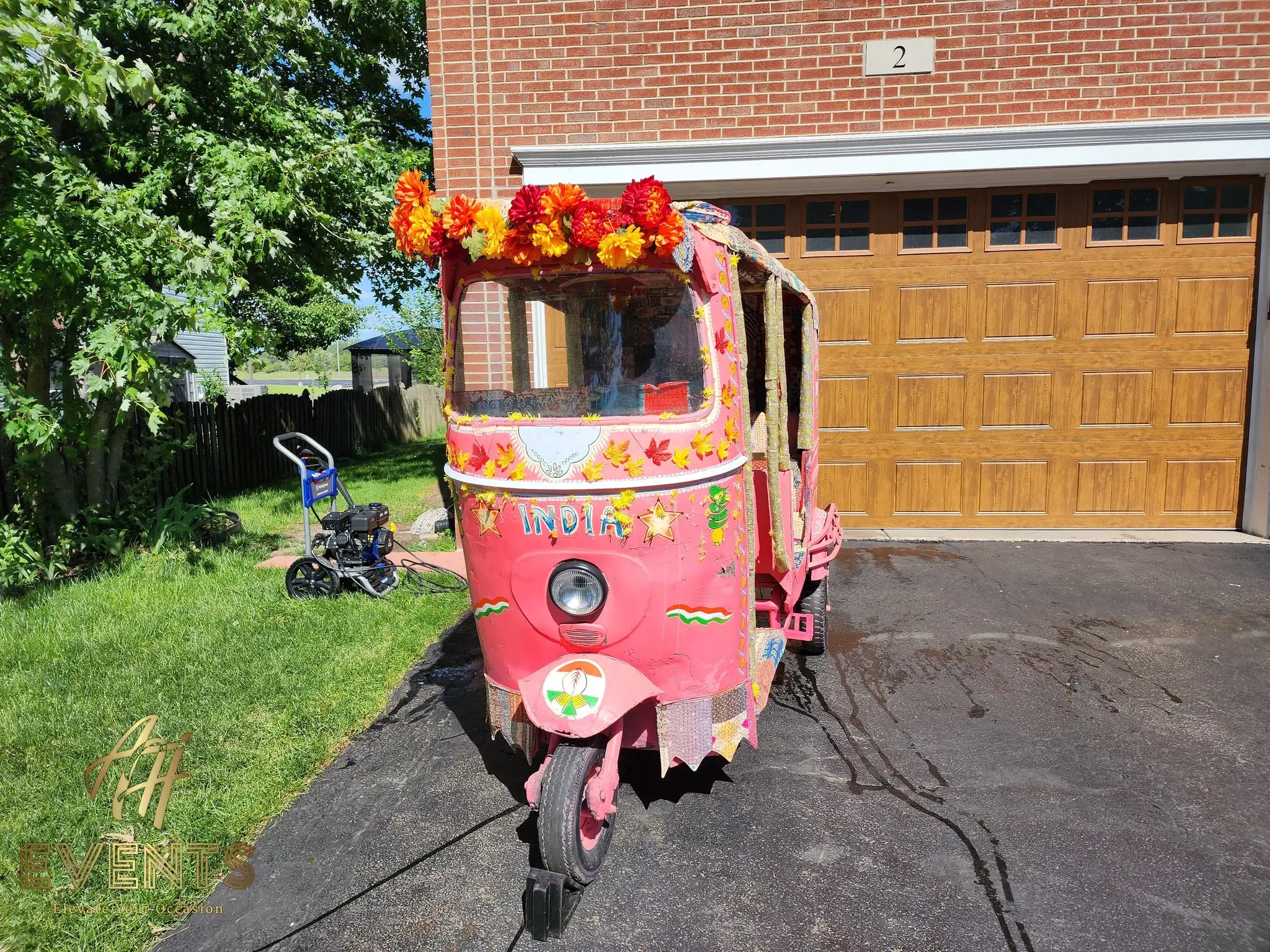 Front view of the pink auto rickshaw topped with orange marigolds in a driveway