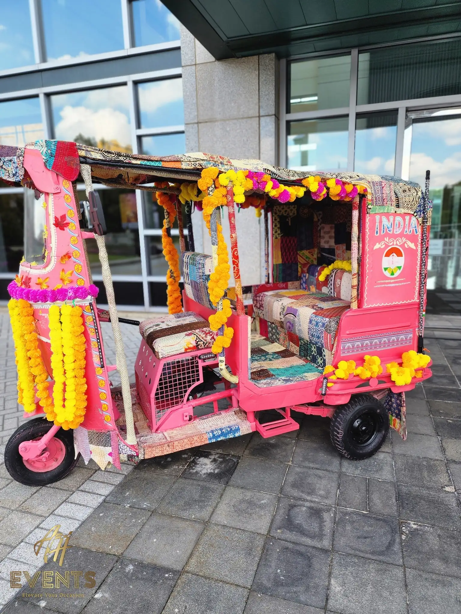 Side view of the marigold-draped auto rickshaw with an 'INDIA' panel, parked on paving stones