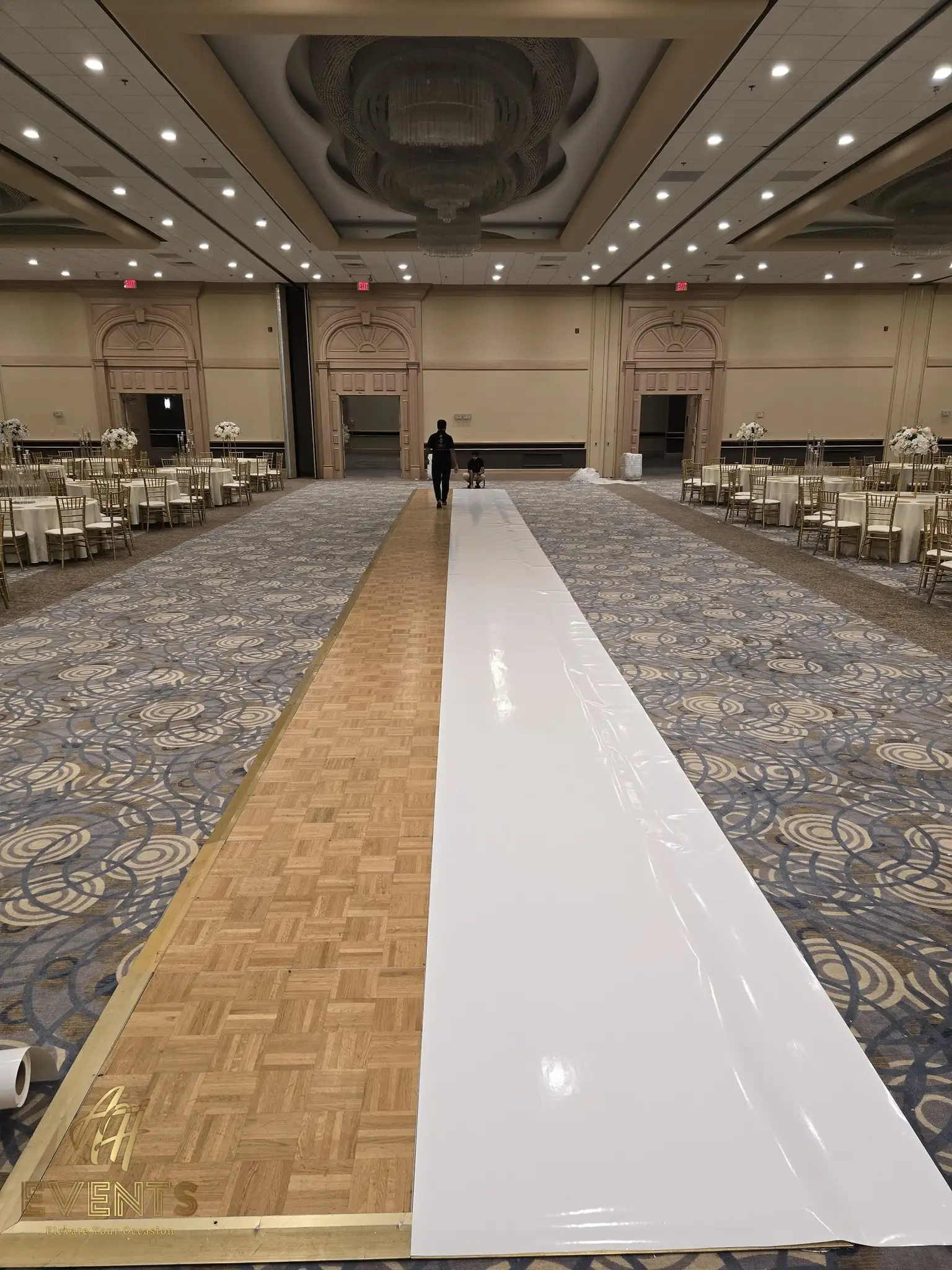 White vinyl aisle being unrolled along a parquet floor in a large ballroom