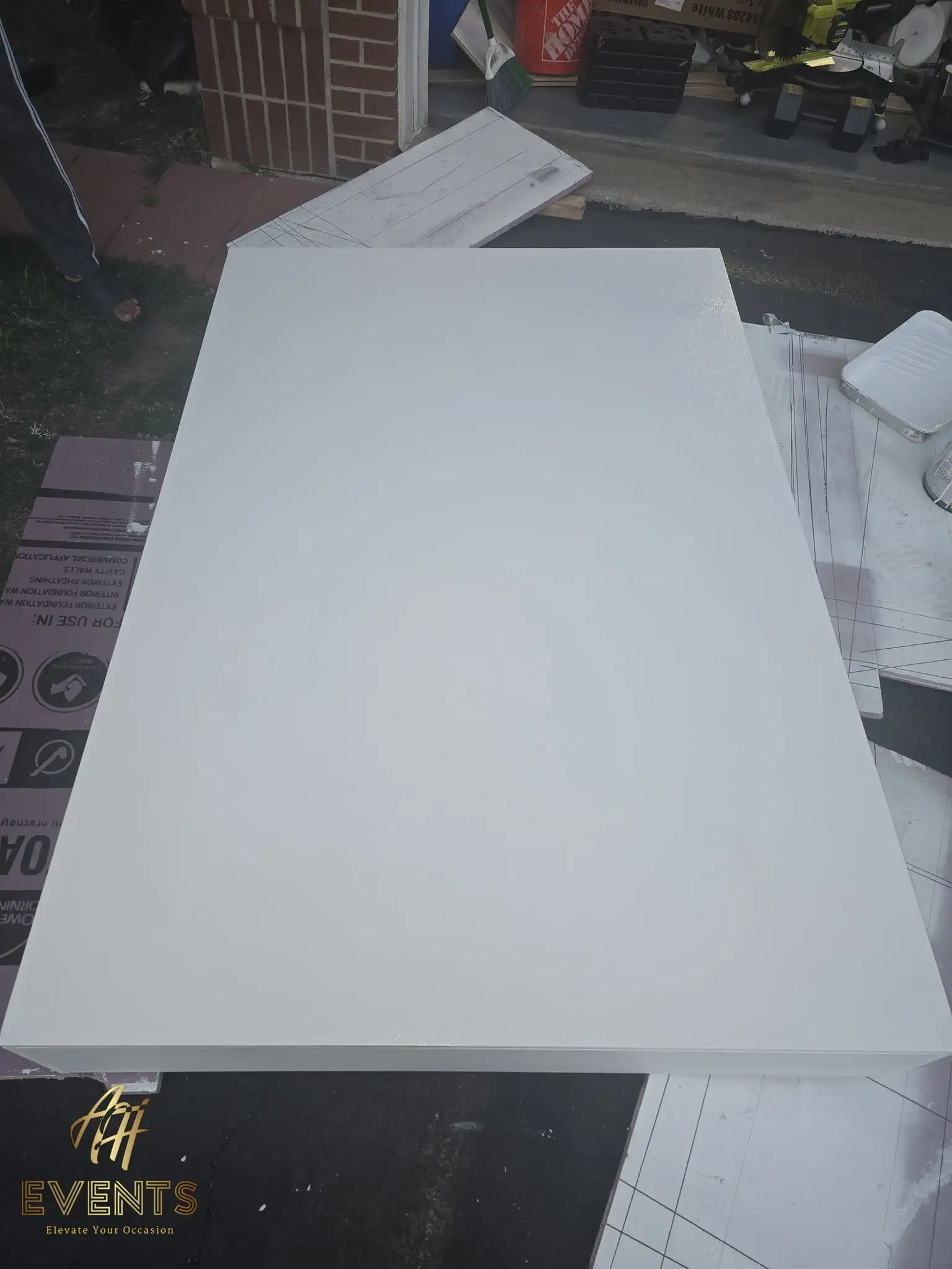 Large flat white-painted platform top resting outdoors by a brick wall, a paint tray beside it