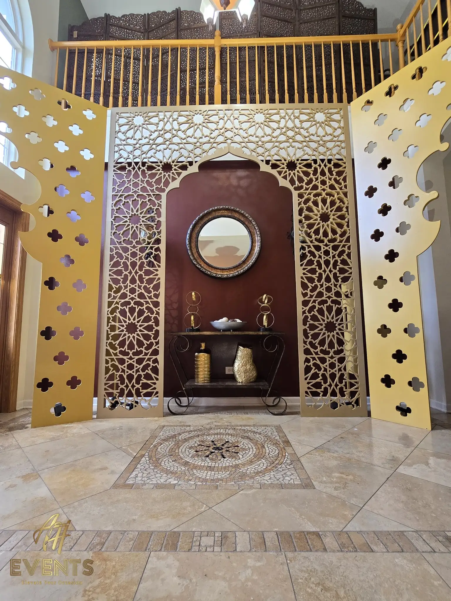 Satin gold quatrefoil-paneled arch with a round mirror and console in a two-story foyer