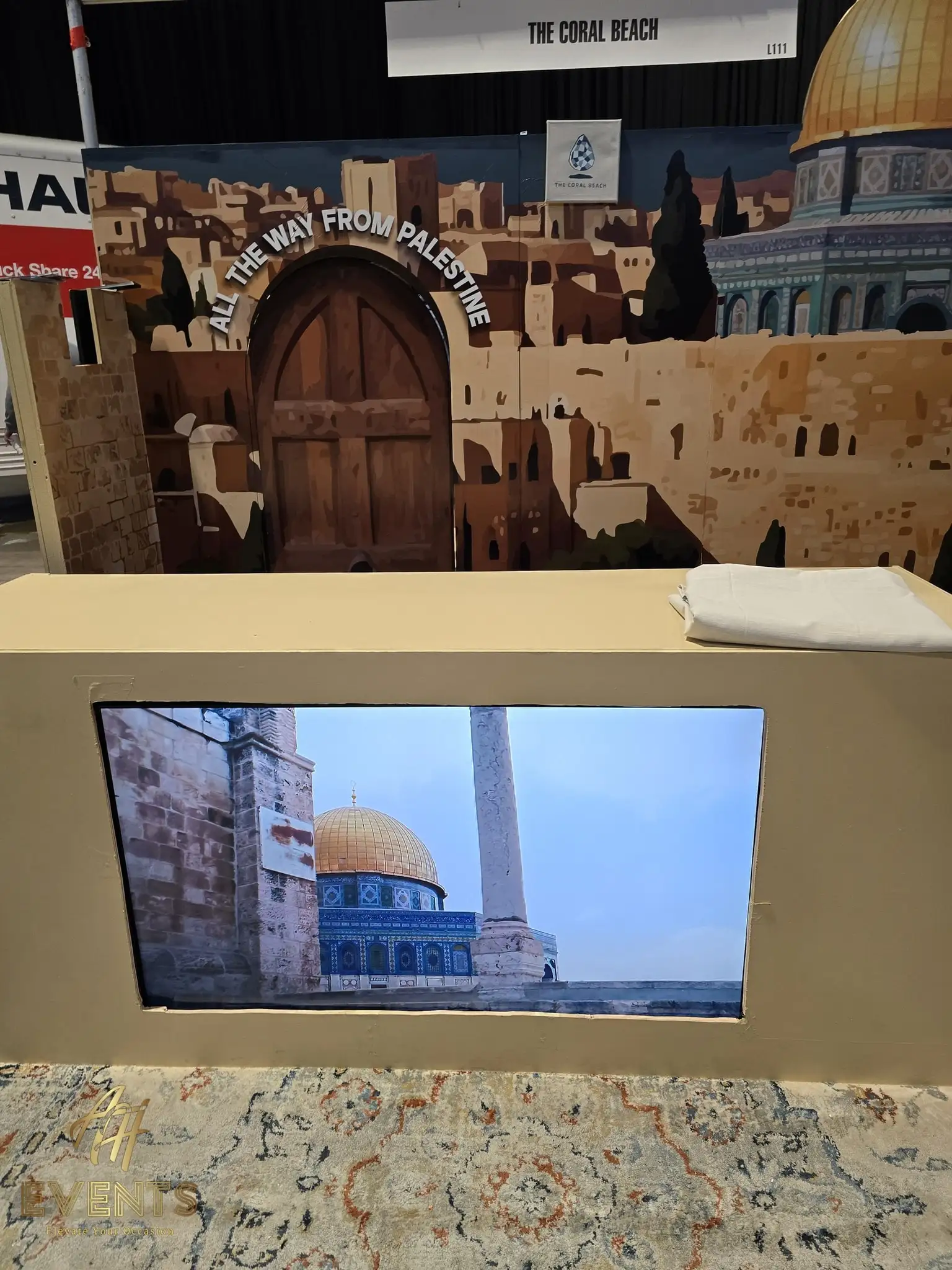 Booth counter with a TV screen showing the Dome of the Rock, beneath the 'All the way from Palestine' mural