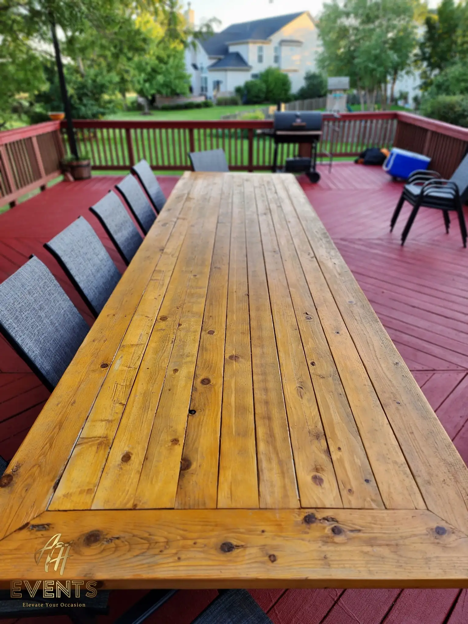 Close view down the wooden plank tabletop showing the grain, gray chairs lining each side on the red deck