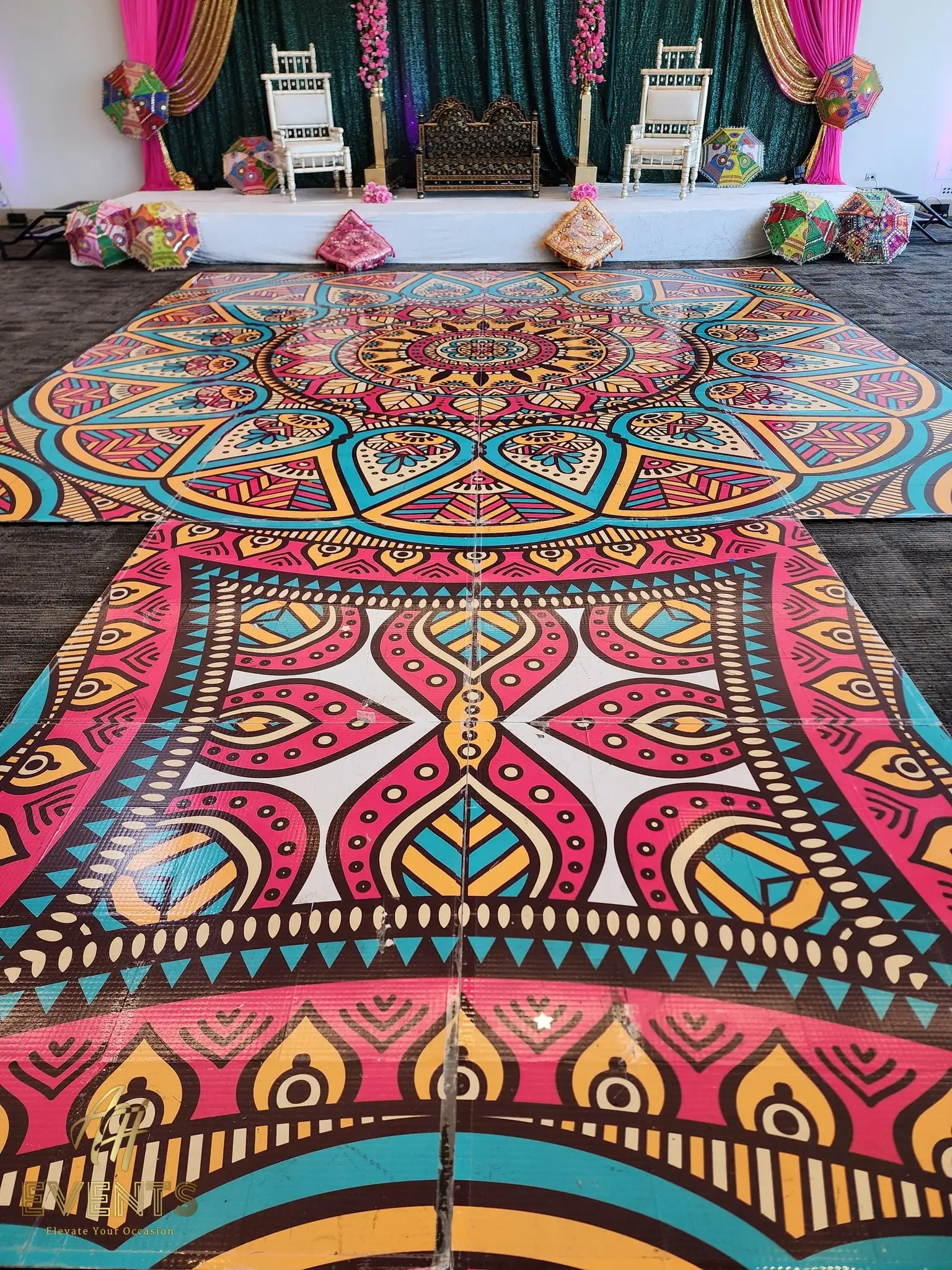 Mandala floor laid in two sections before a stage with white chairs and hanging paper lanterns