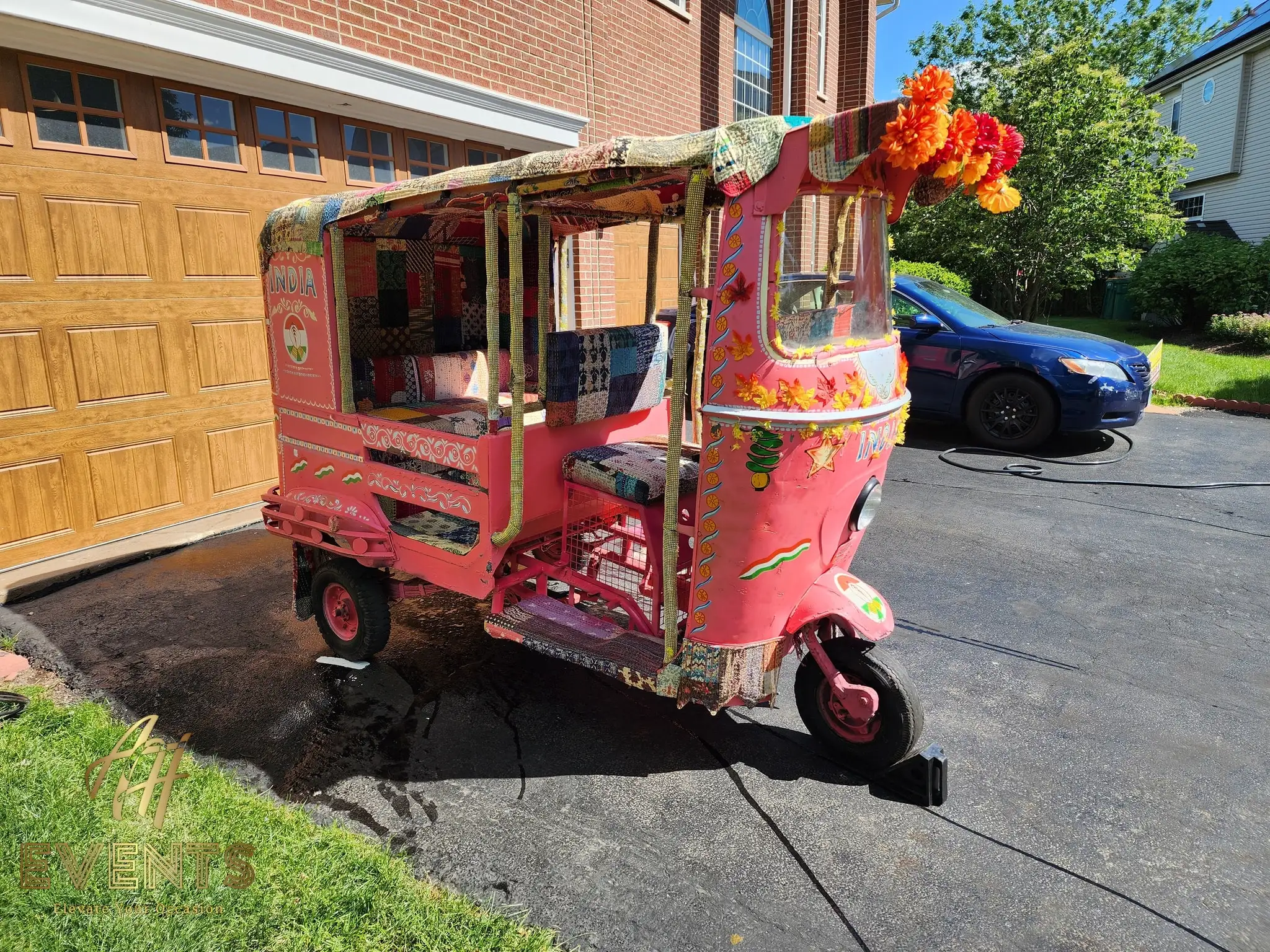 Three-quarter view of the decorated pink auto rickshaw with marigolds on its roof in a driveway