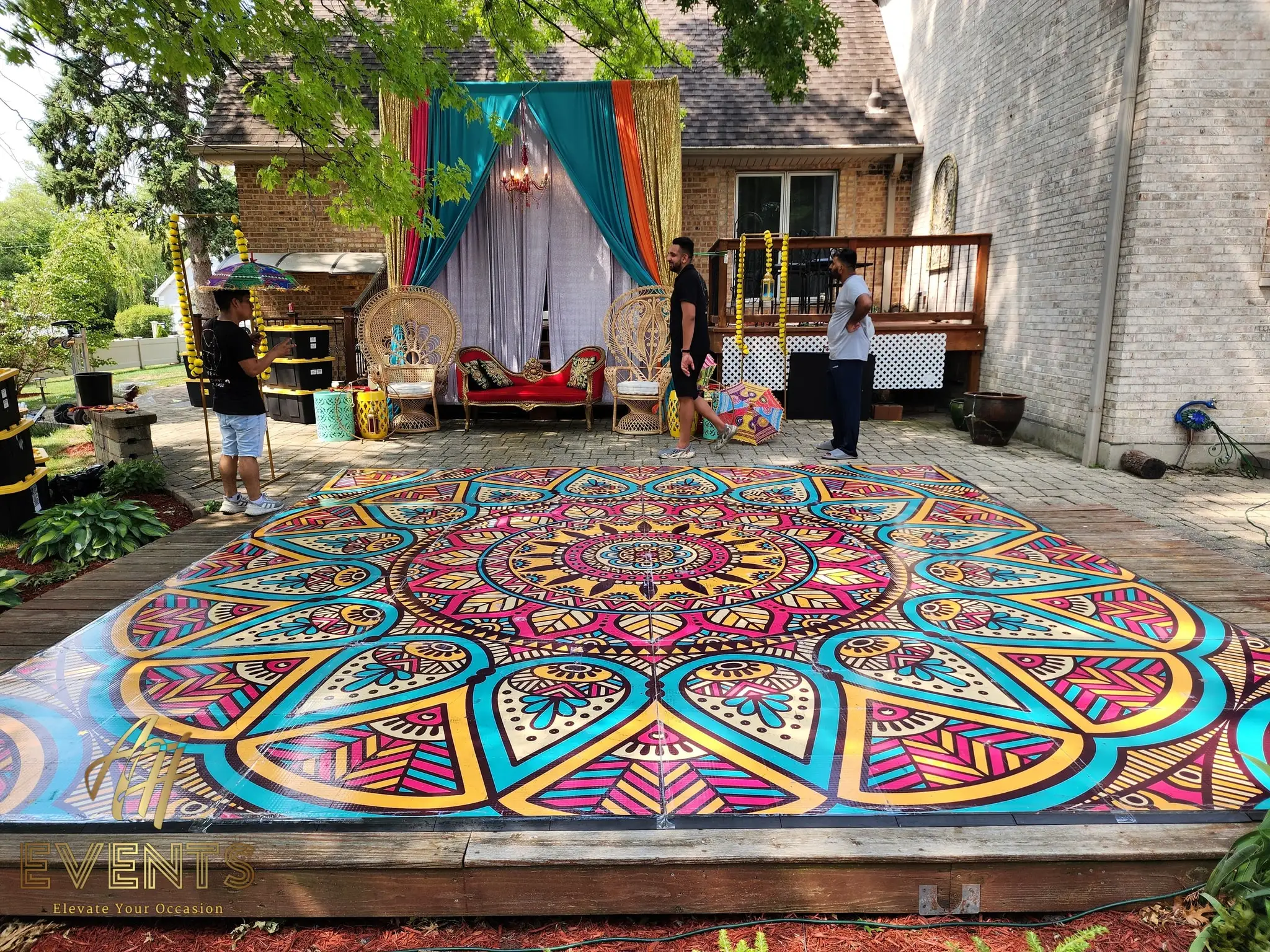 Mandala floor on a deck with a teal-and-gold drape backdrop and guests nearby