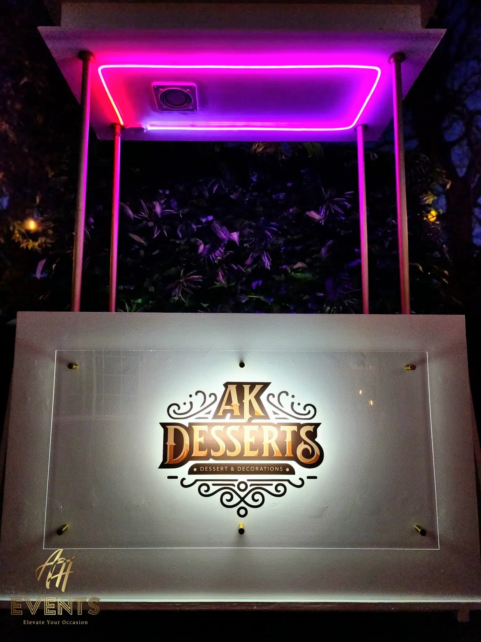 AK Desserts cart at night with its canopy glowing magenta and the logo panel backlit white