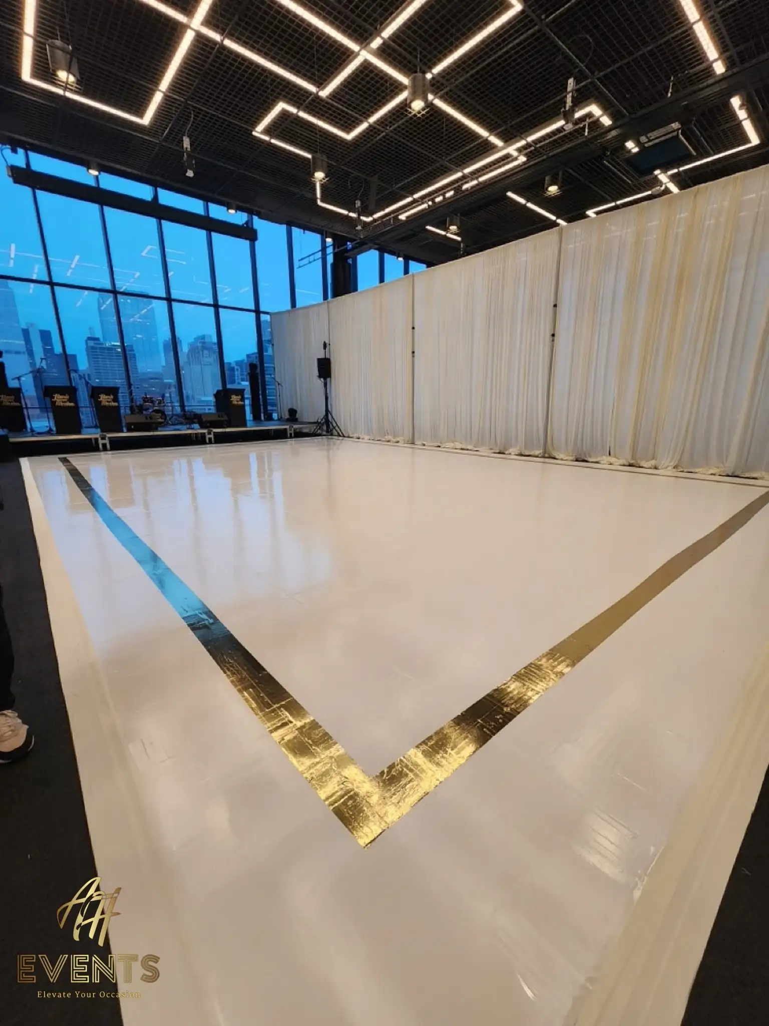 White dance floor with a gold mirror L-corner border, city skyline through the loft windows