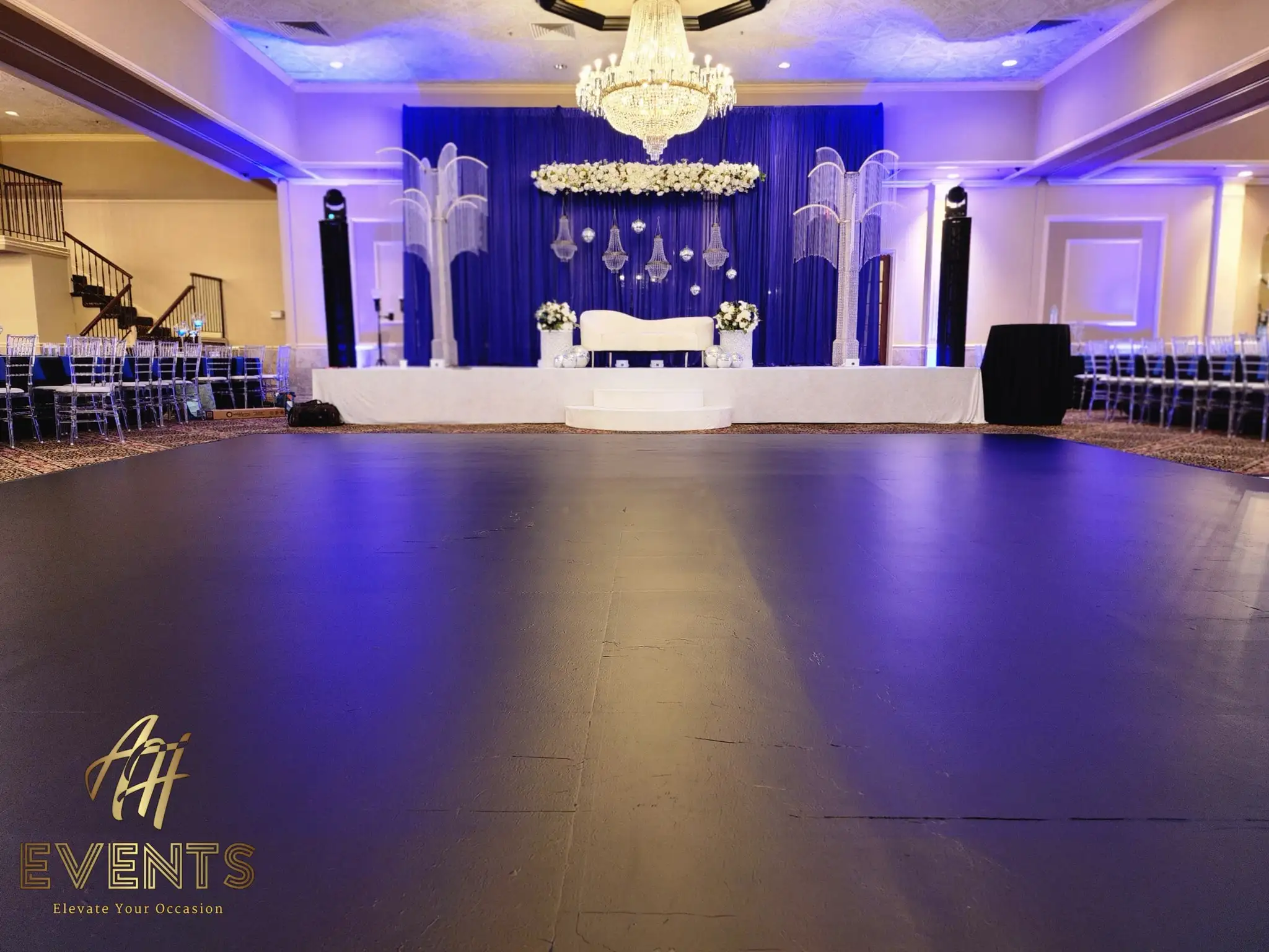 Low view across the black dance floor toward a navy stage with white florals and crystal palm columns under a chandelier