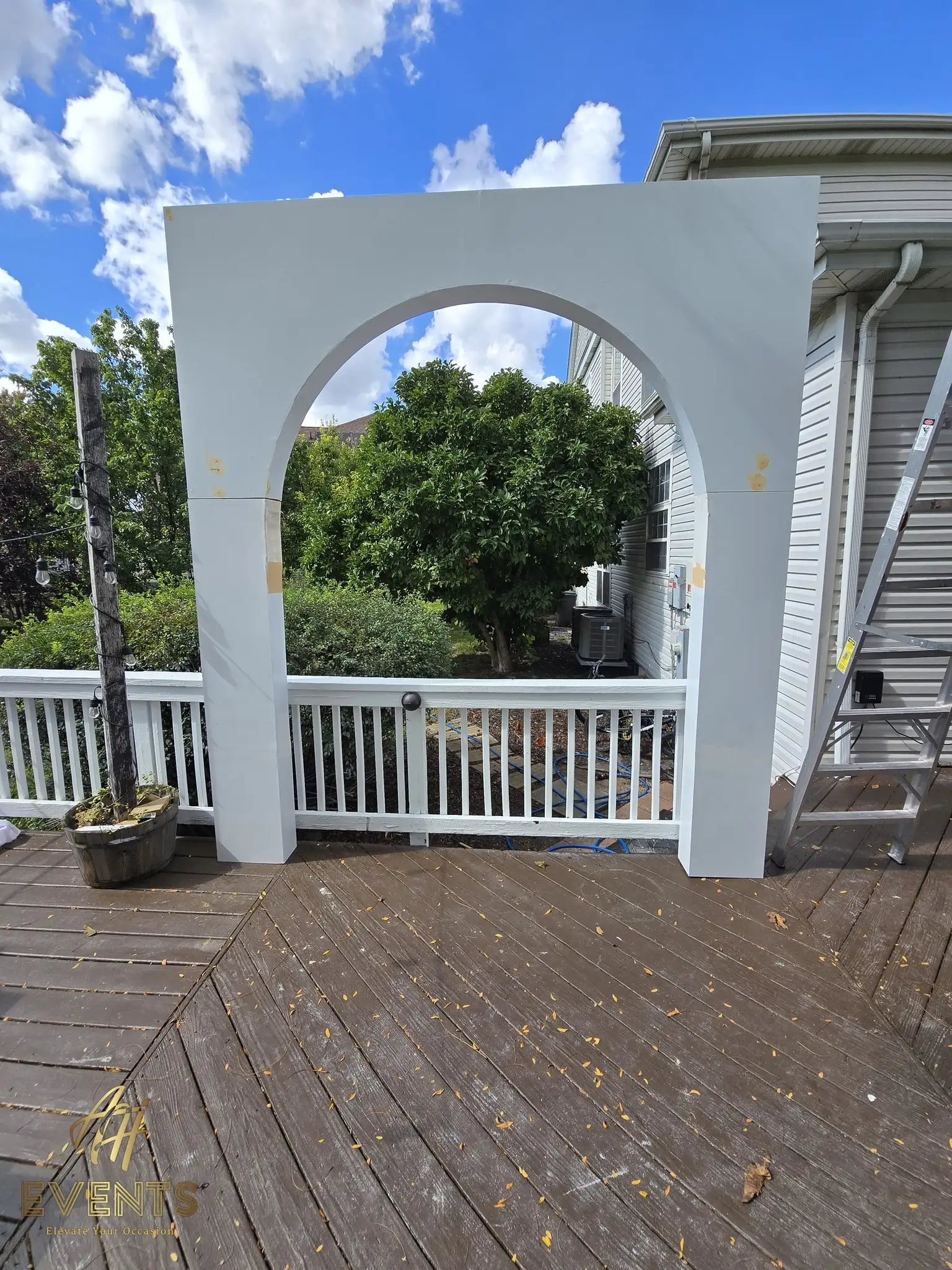 White arch with a rounded opening on a deck under a blue sky during setup