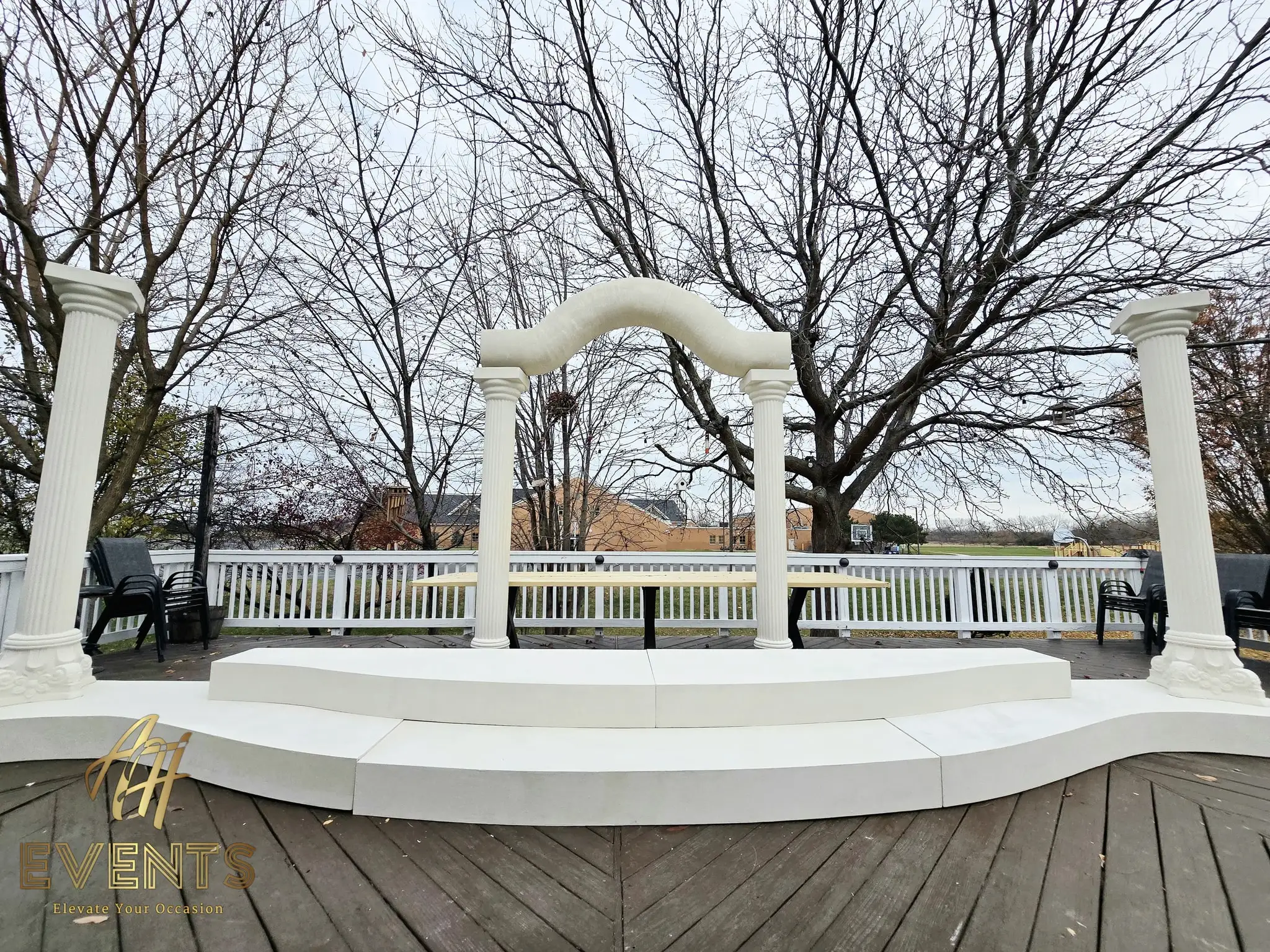 Finished classical-pillar wedding stage on a deck — fluted columns and a serpentine arch over a curved riser, chairs to the sides