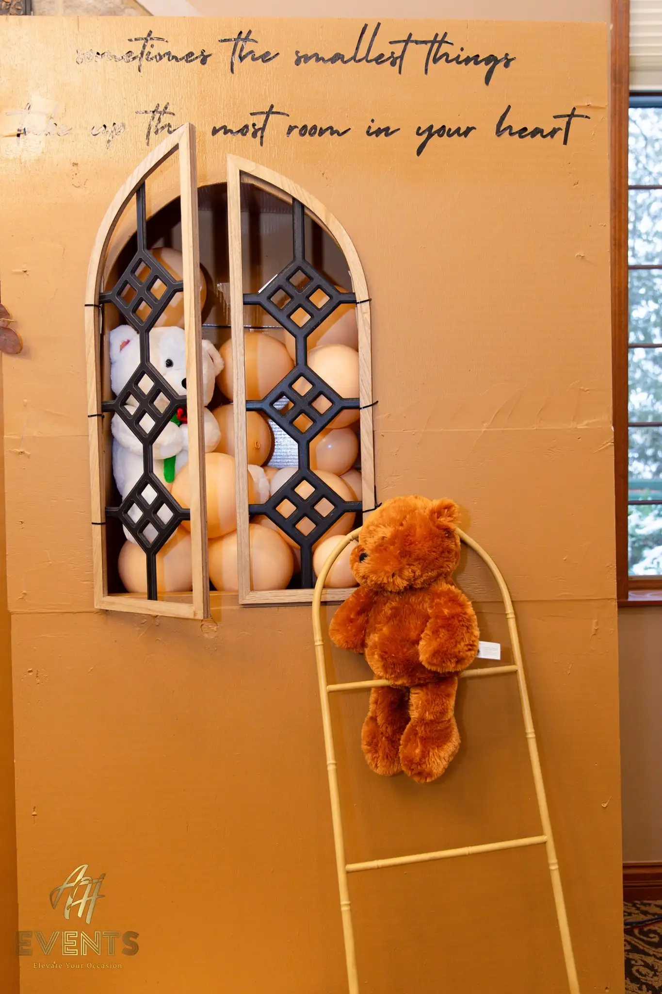 Gold storybook house backdrop reading 'sometimes the smallest things take up the most room in your heart', with a teddy in the window and one on a ladder