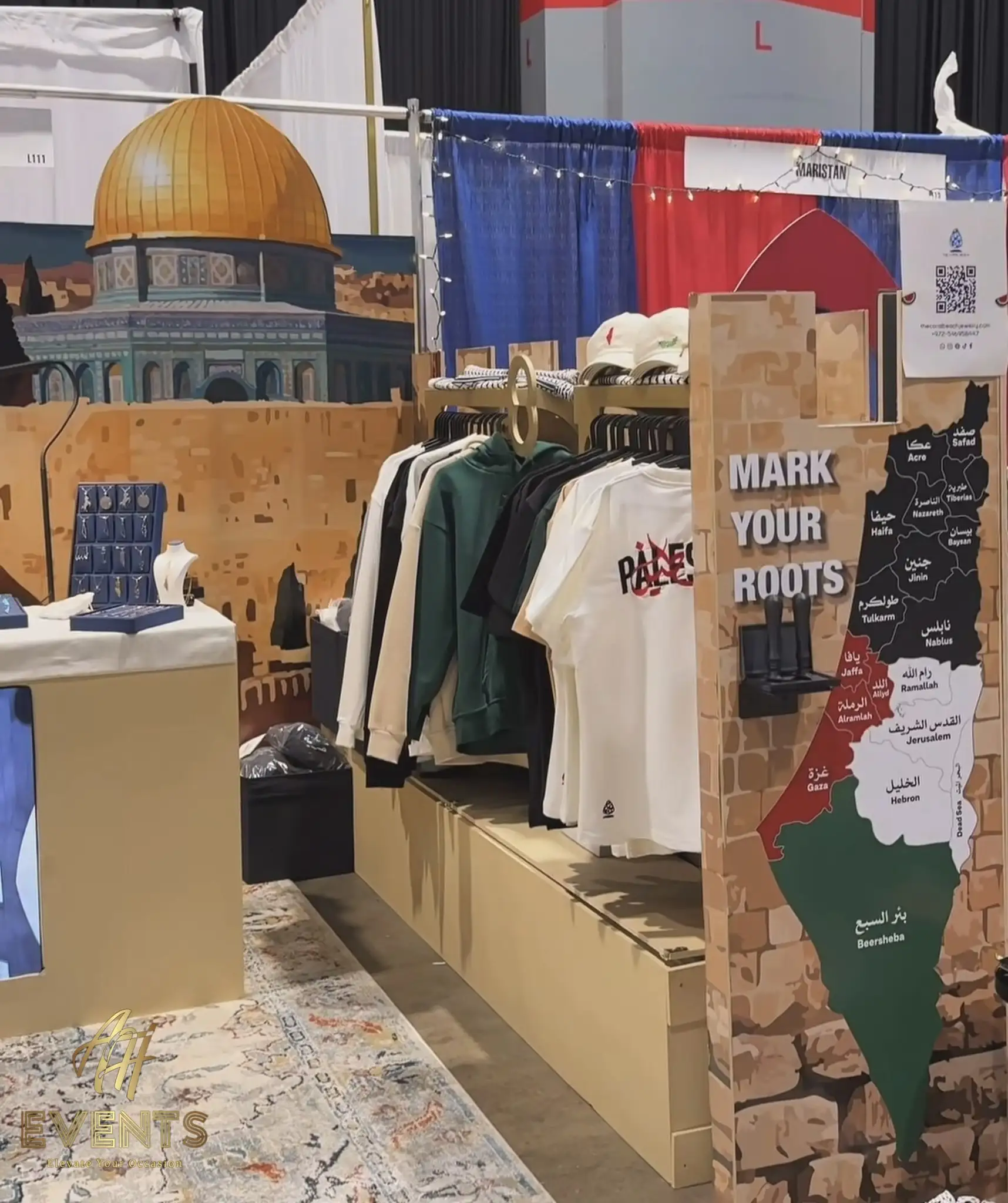 Apparel display on the Coral Beach booth platform with the 'Mark Your Roots' map panel and Jerusalem mural