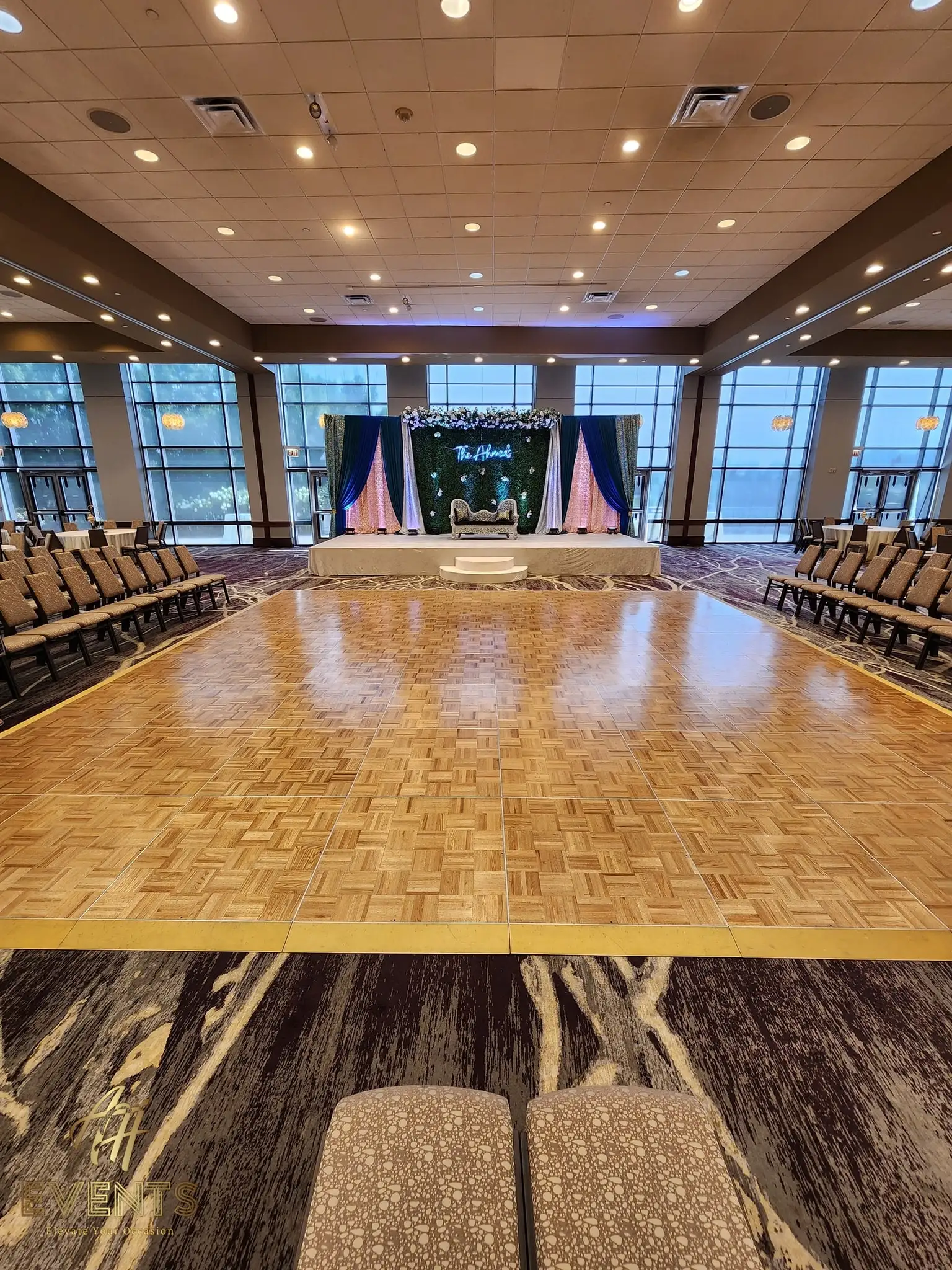 Parquet wood dance floor in a window-lined ballroom facing a blue-and-pink draped stage