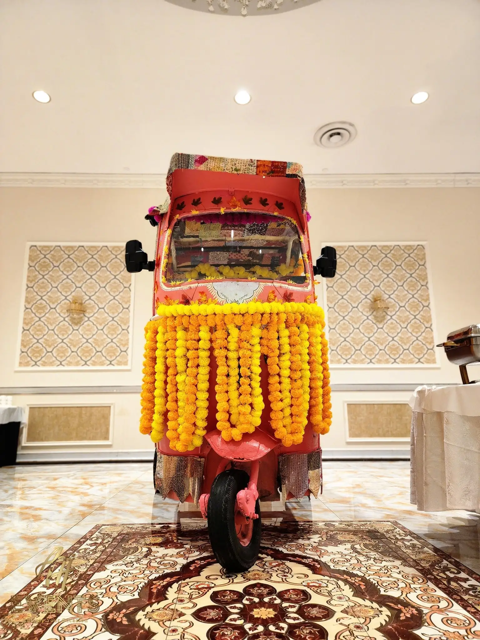 Front of the auto rickshaw with marigold garland curtains displayed on an ornate rug in a banquet hall