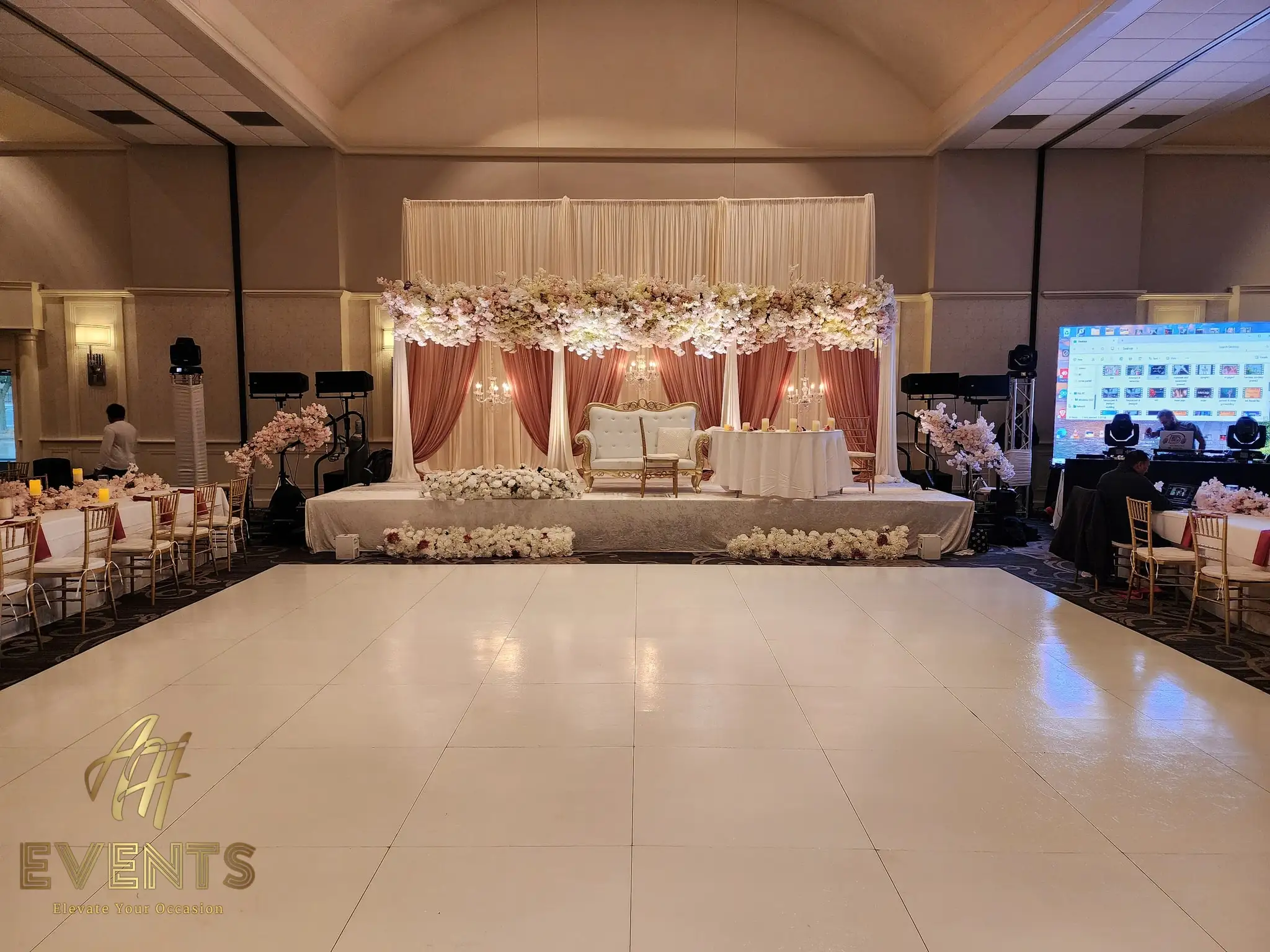 White dance floor before a mauve-and-ivory stage with a gold loveseat under a blush floral canopy