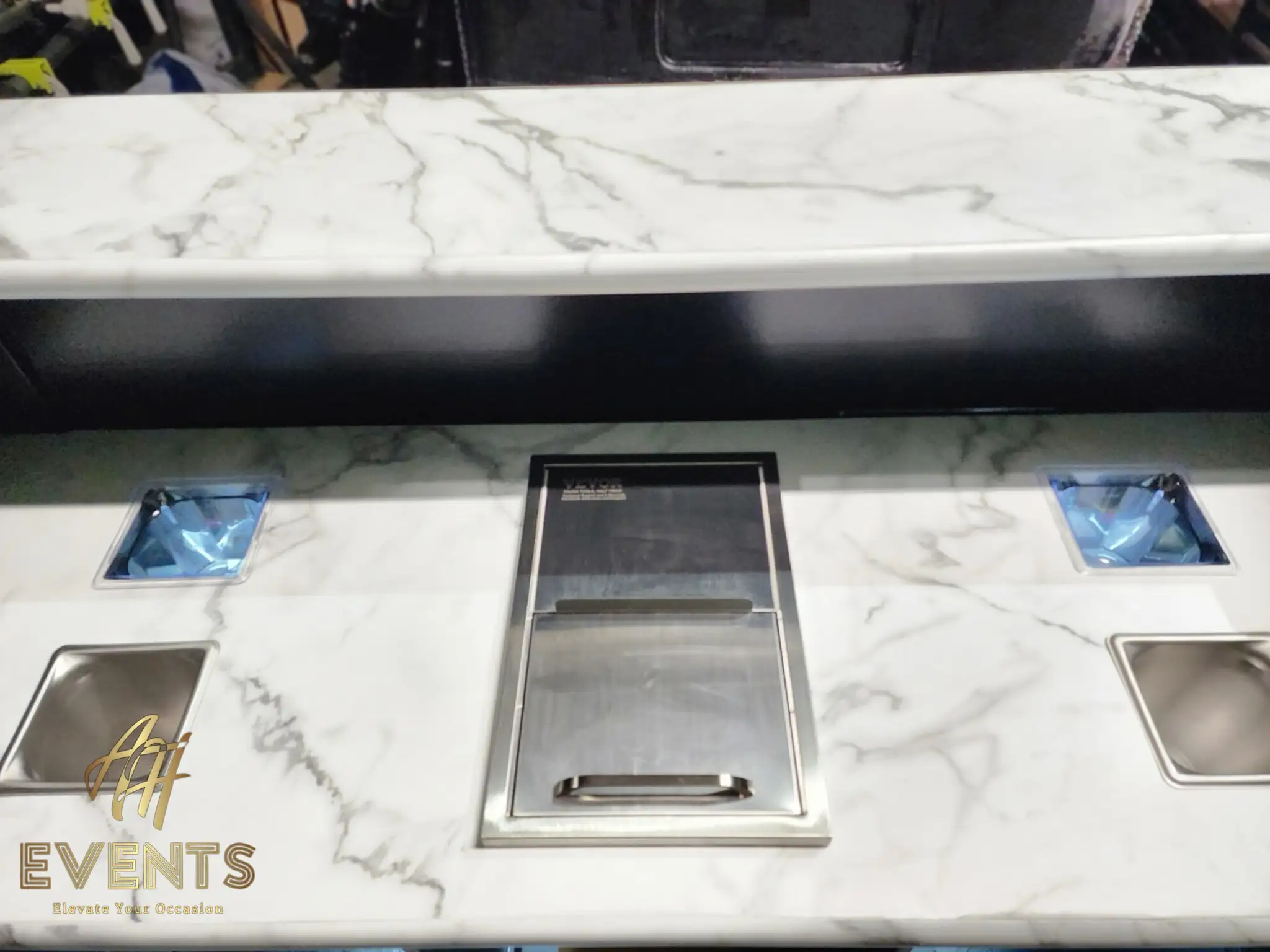 Marble counter detail of the Bobawala cart with blue-lined condiment pans flanking a recessed stainless cup dispenser