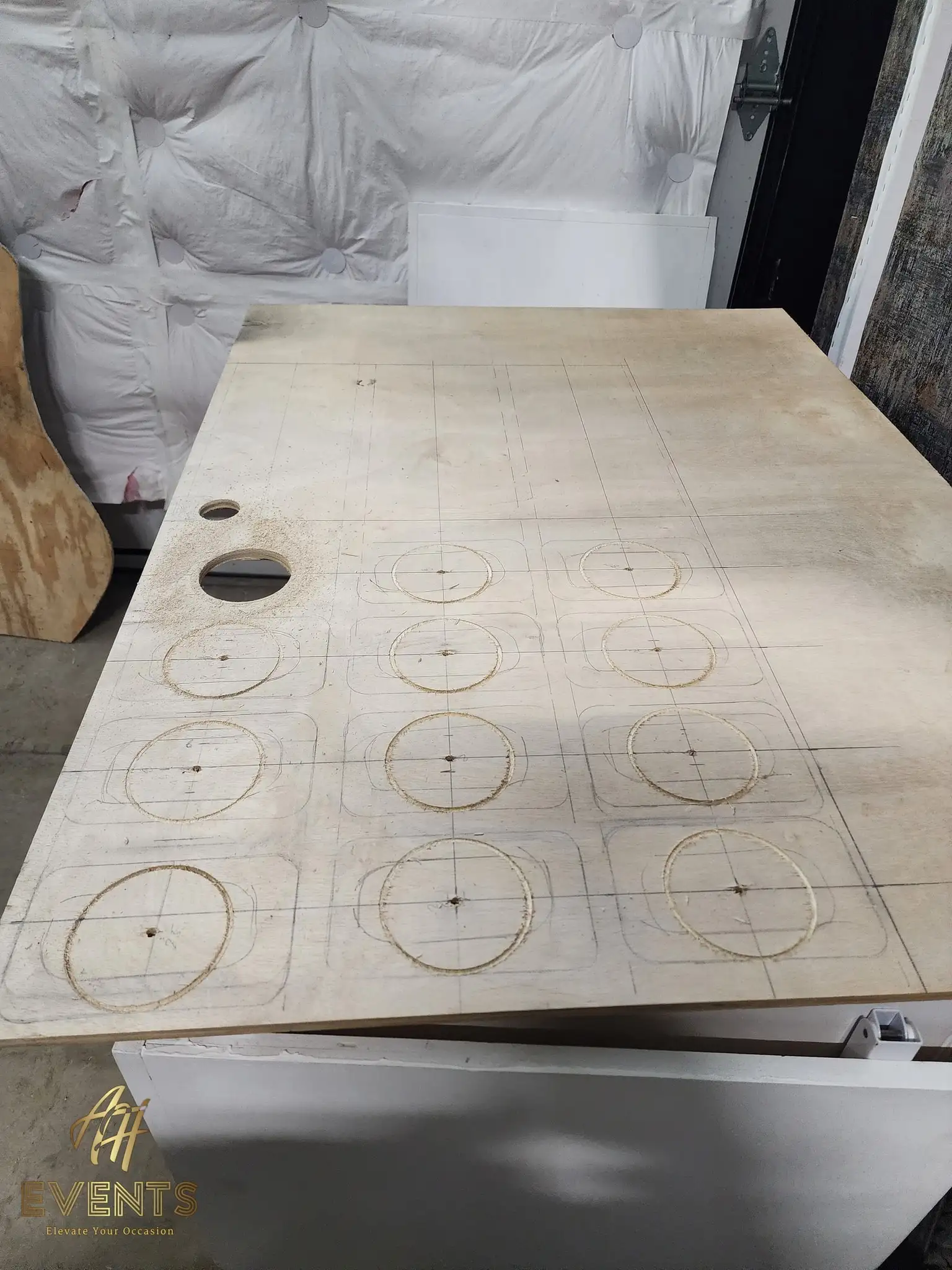 Plywood cart top with routed circle outlines and pilot holes across a penciled grid, sawdust on the surface