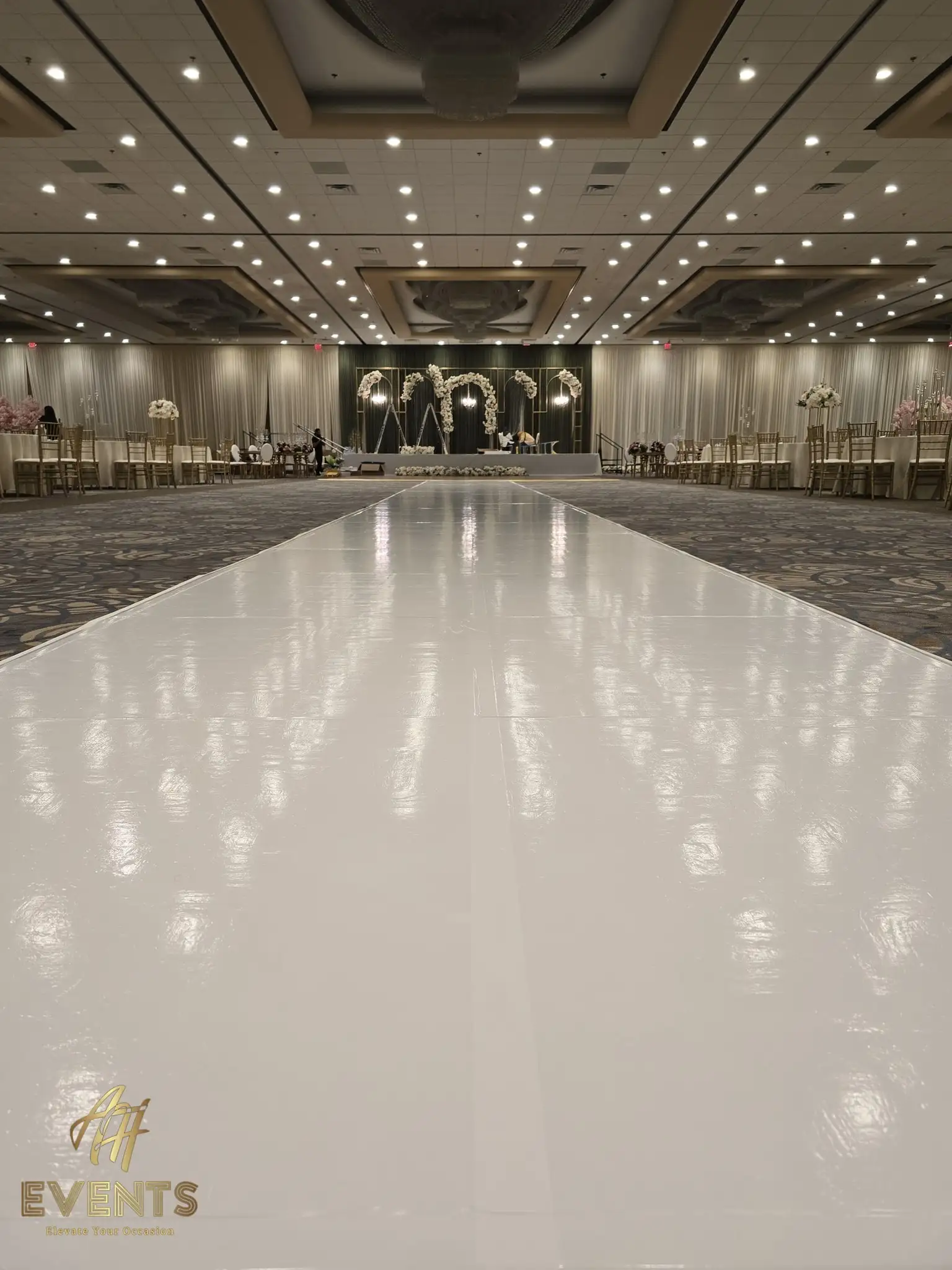 Straight-on view of a glossy white vinyl aisle leading to a lit floral arch wedding stage