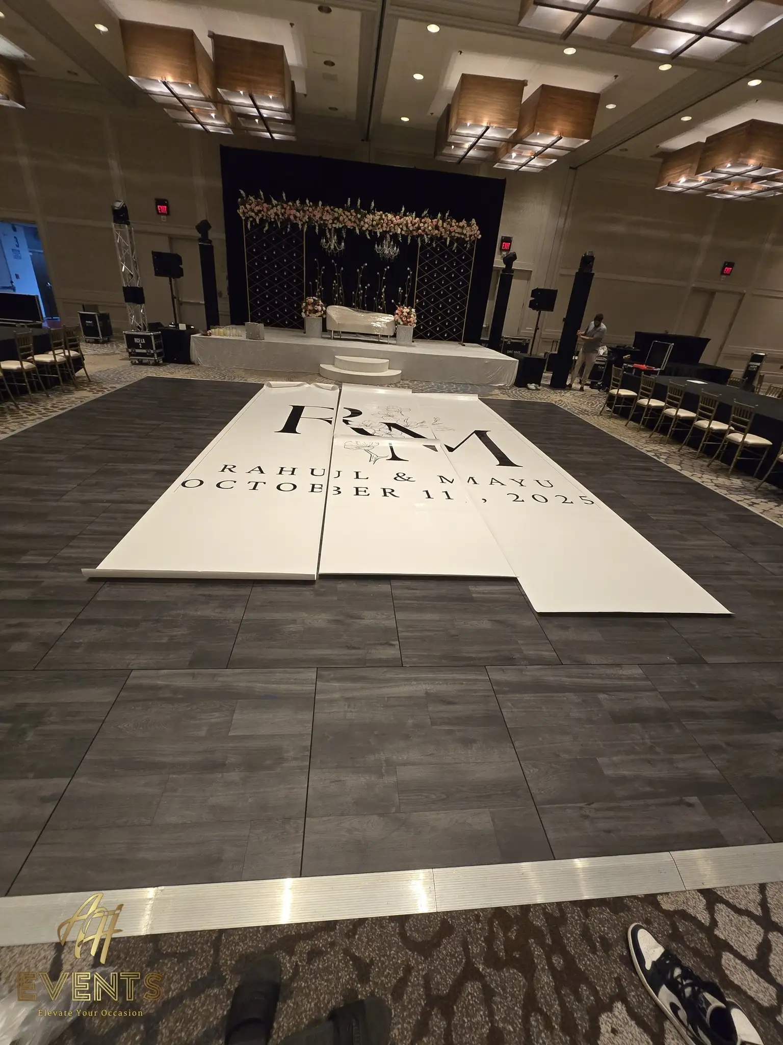 Sections of the 'R M — Rahul & Mayu, October 11, 2025' monogram floor laid out over gray planks during installation