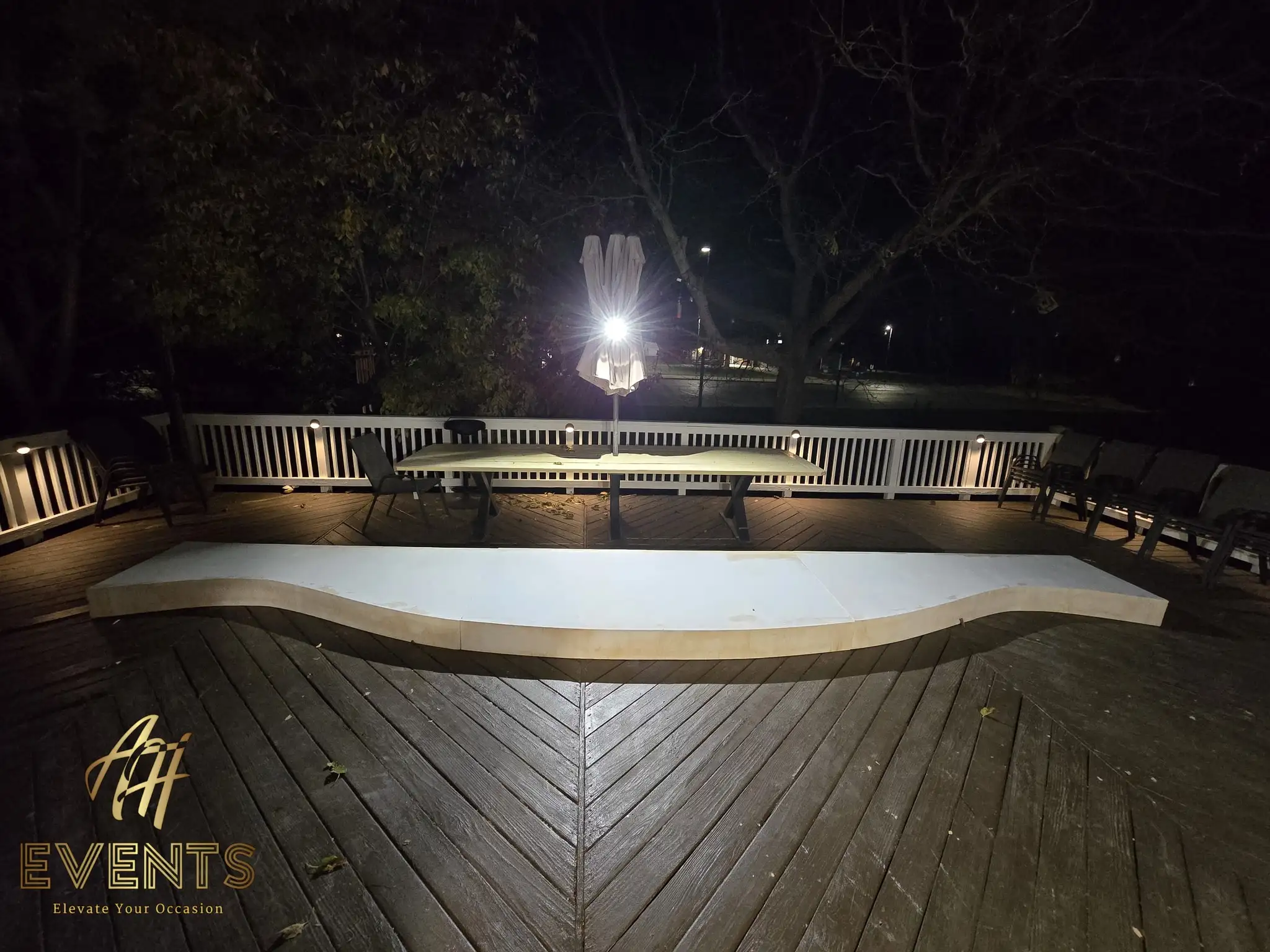 Curved white stage riser on a deck at night, lit, with a folding worktable behind