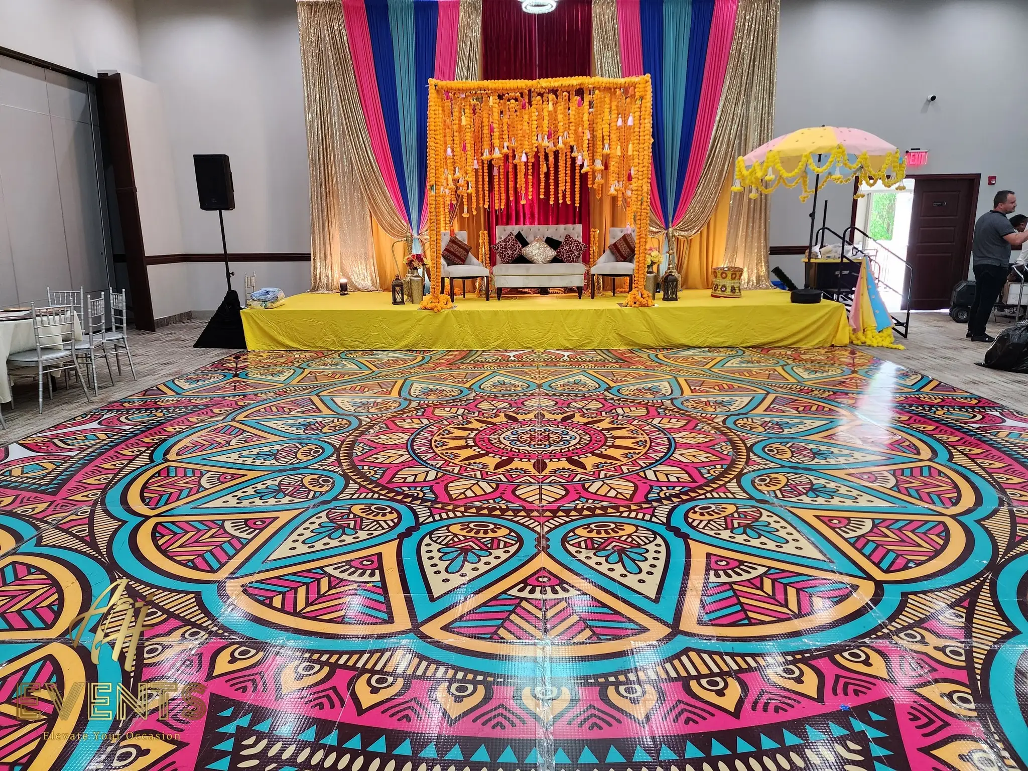Mandala floor before a gold and pink draped stage trimmed with yellow marigolds