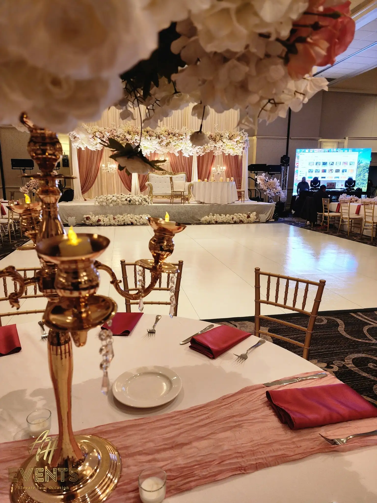 Reception table with a gold candelabra and red napkins, the white floor and blush floral stage behind