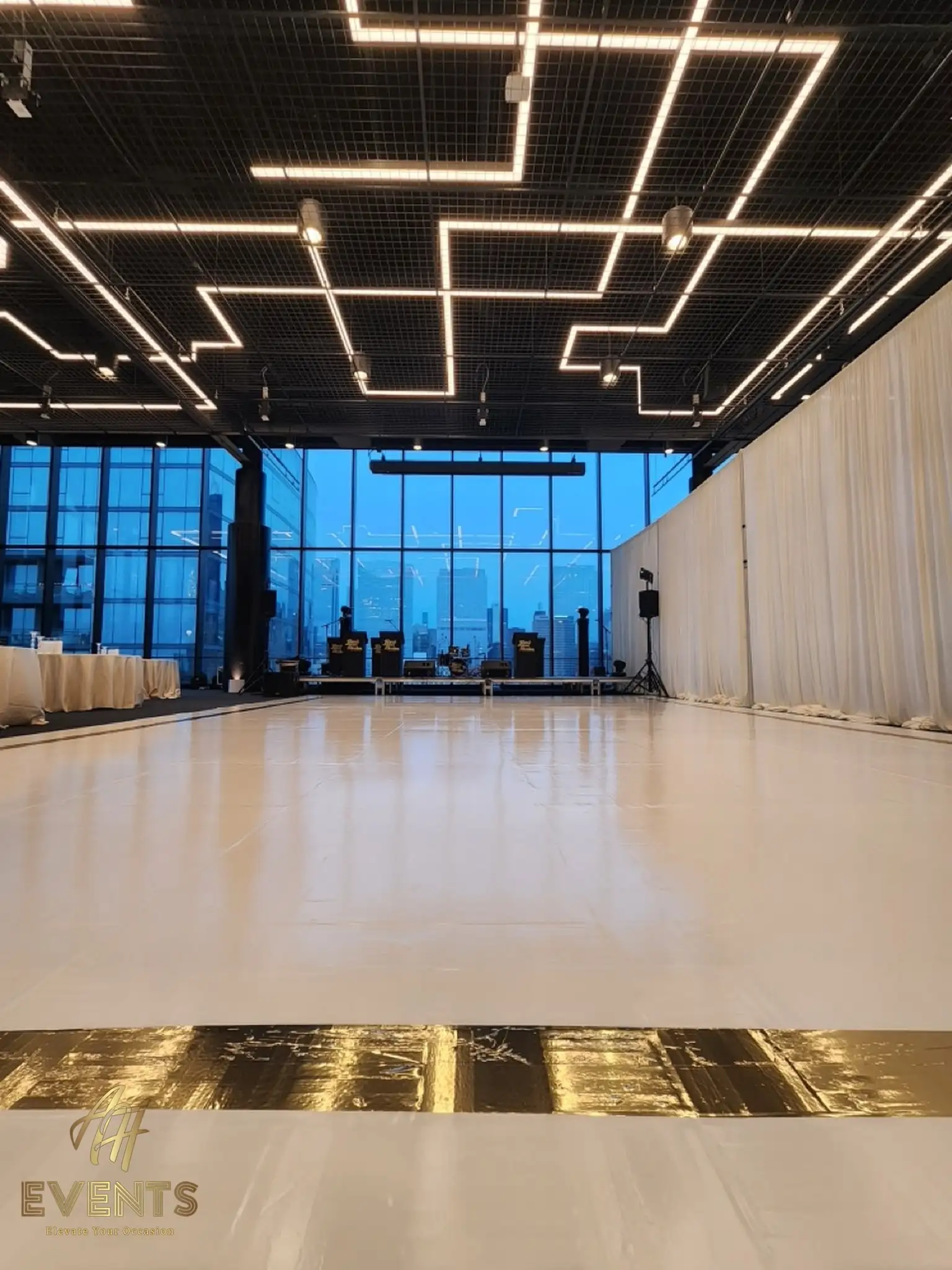 White dance floor with a gold stripe in the loft under hexagonal light fixtures, band stage and skyline behind