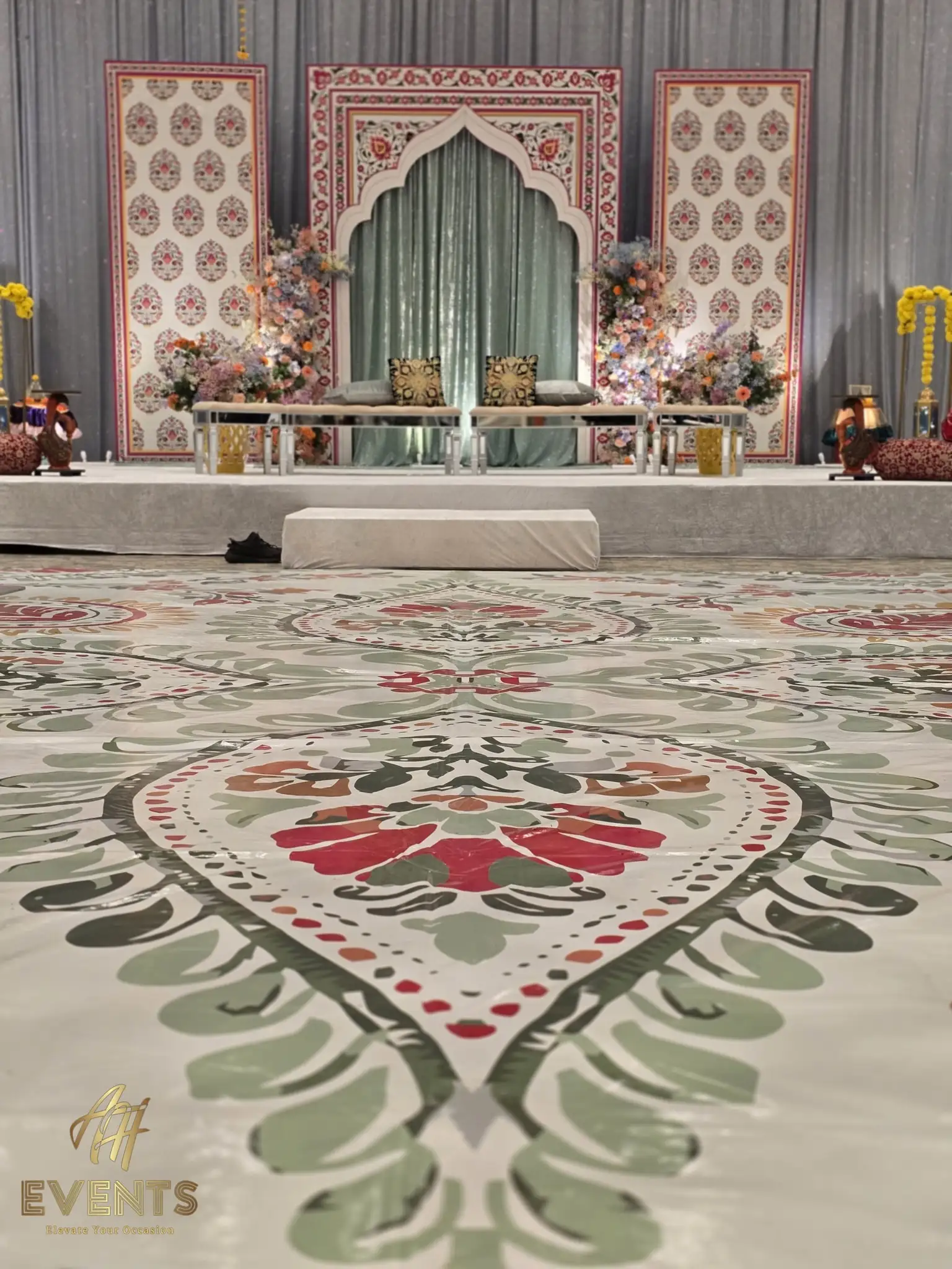 Decorated stage with an arched backdrop and sage drapes above a green-and-red floral flex vinyl floor