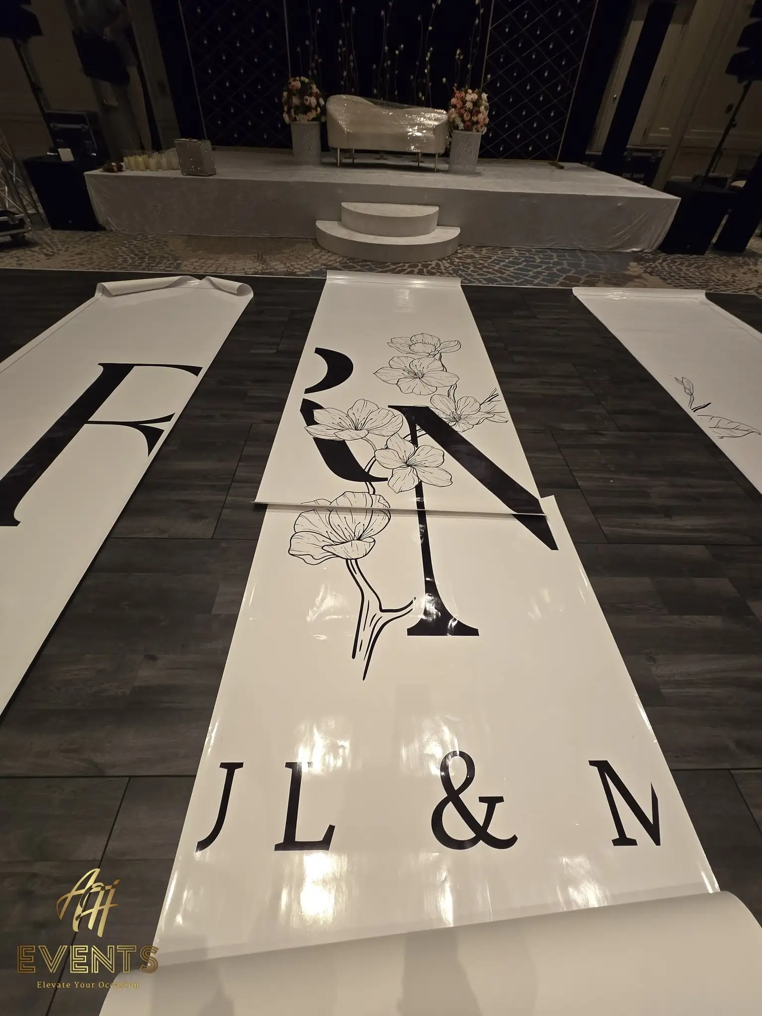 Printed monogram floor panels with magnolia artwork and serif lettering laid out and being aligned during setup, the lattice stage behind