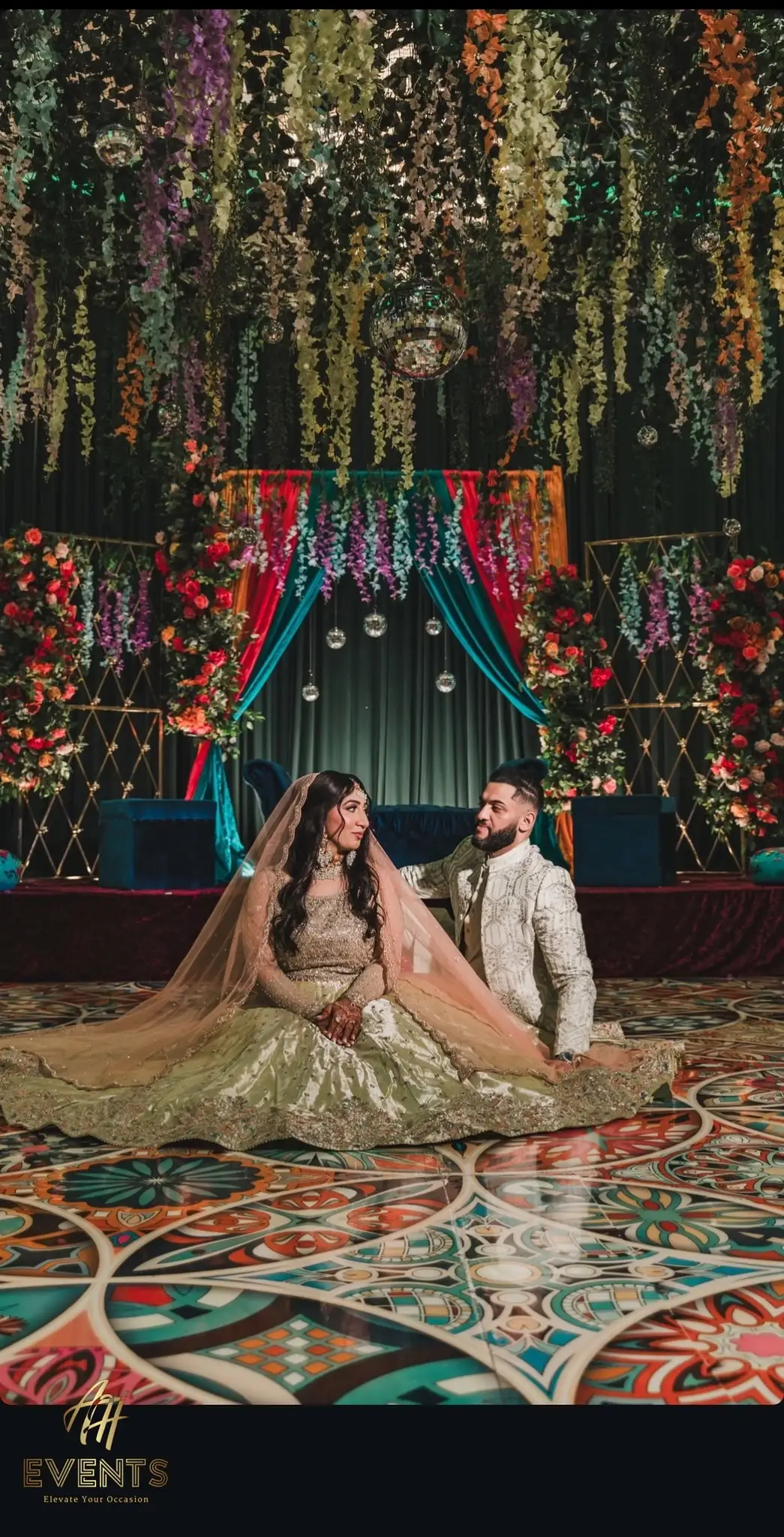 Couple seated on a floral stage above the Kaleidoscope floor, with hanging florals overhead