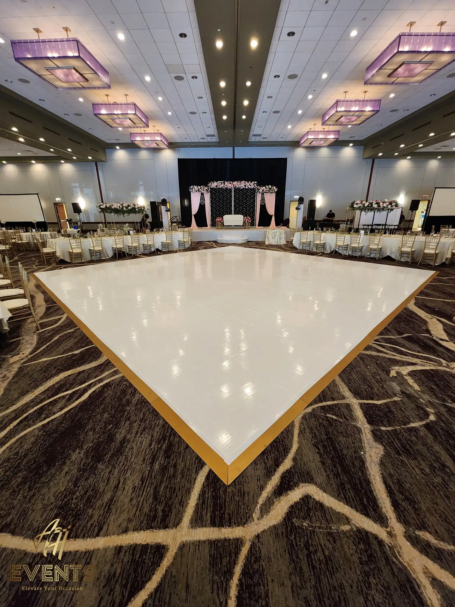 Glossy white dance floor with a gold-trim border facing a pink-lit stage on a swirl-patterned carpet