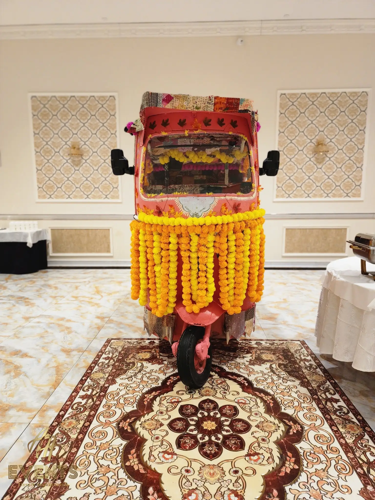 Auto rickshaw with cascading marigold garlands displayed in a banquet hall on a patterned rug