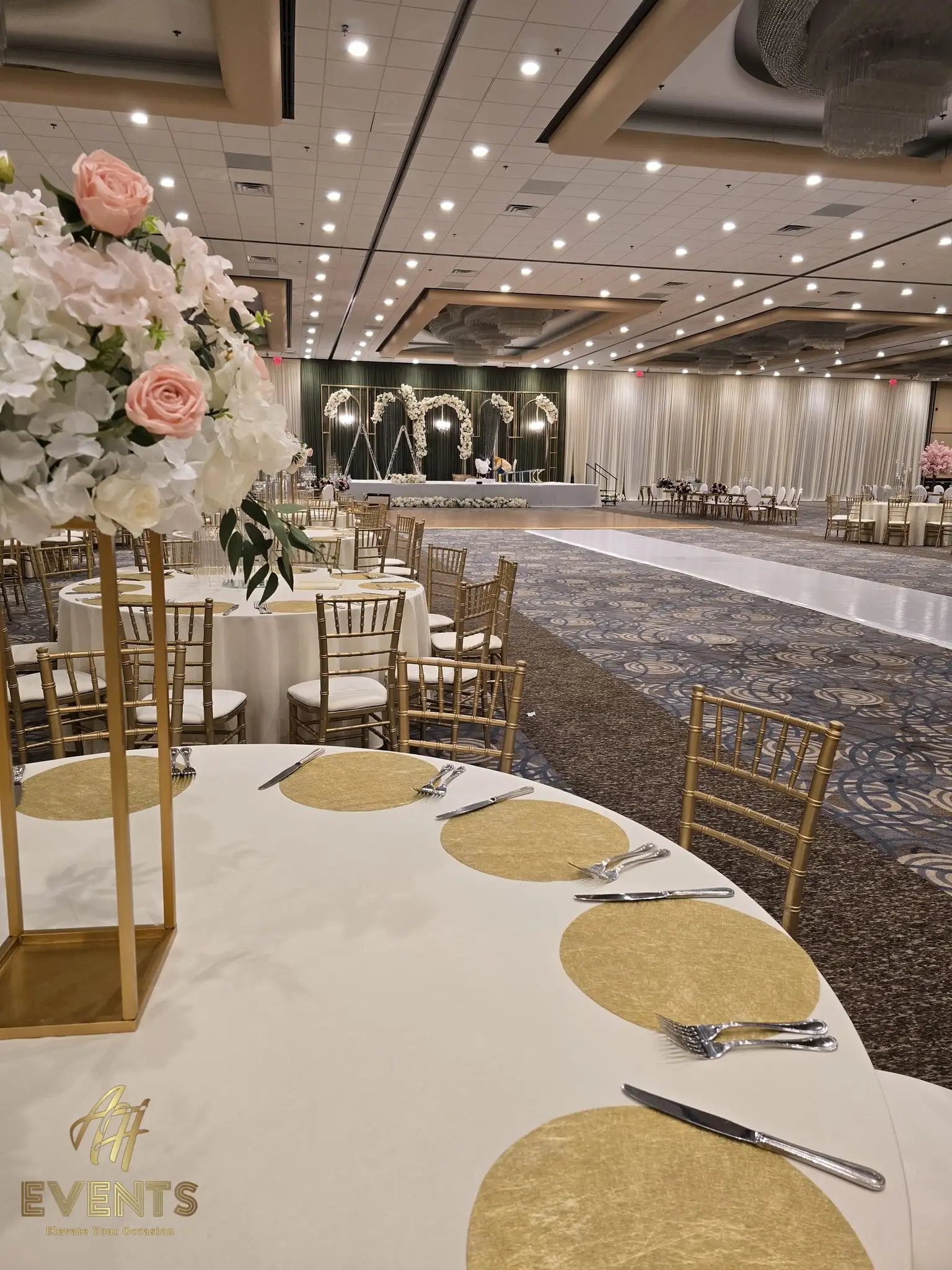 Banquet table with a pink-and-white floral centerpiece beside the glossy white aisle and floral arch stage