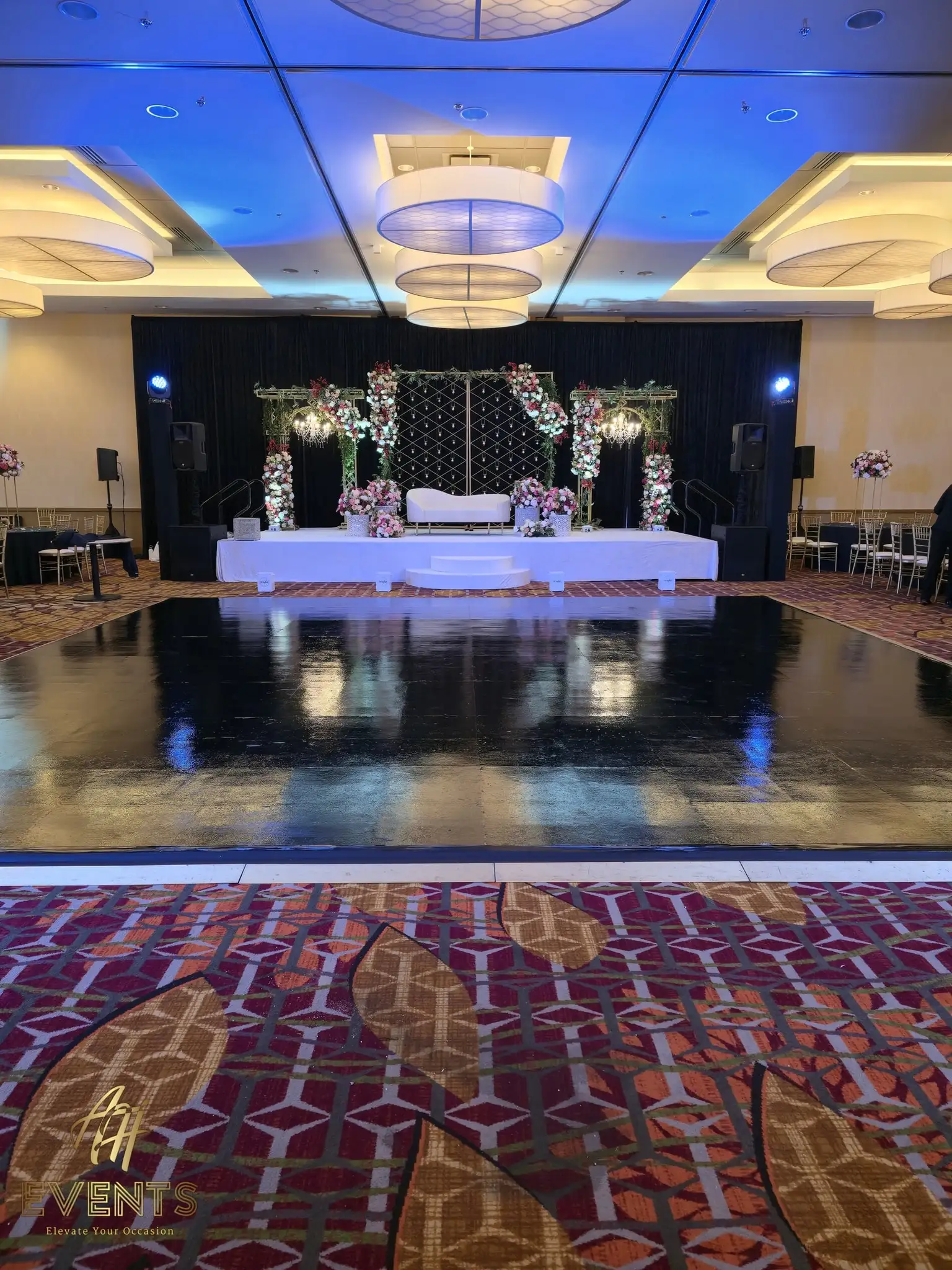 Black dance floor reflecting the white floral mandap stage in the ballroom