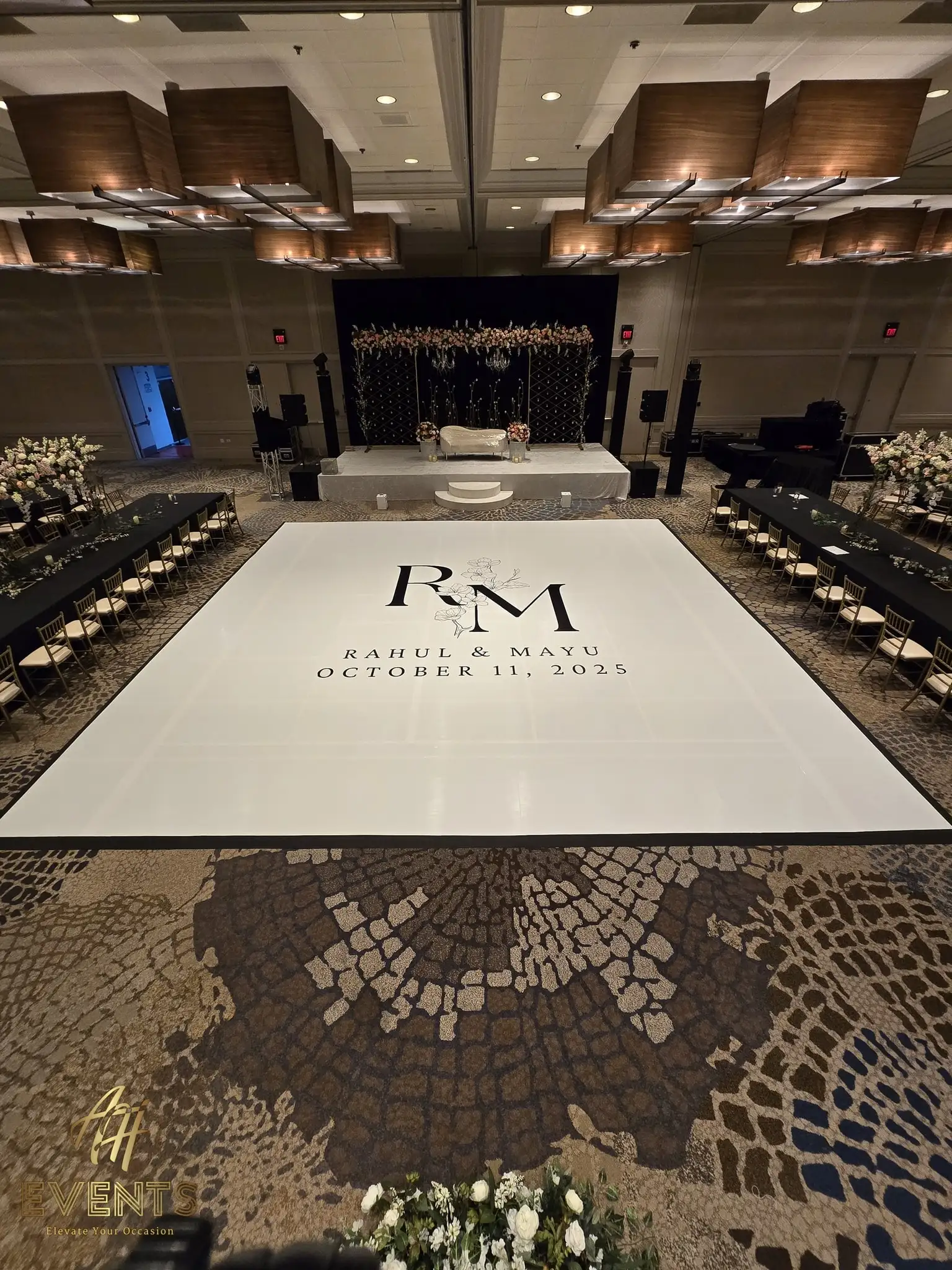 Glossy white 'R M' monogram dance floor with white florals at the corner, the black lattice stage behind