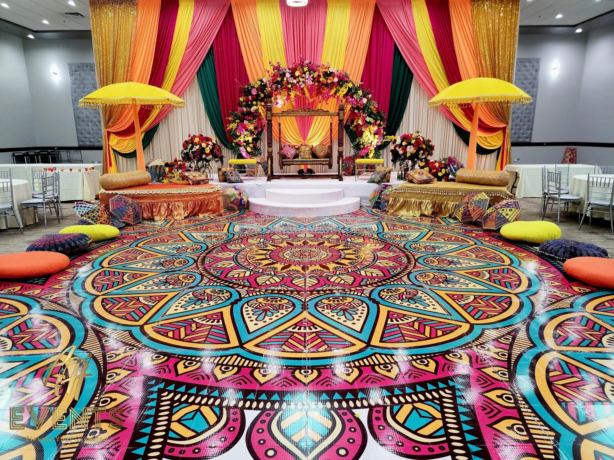 Mandala floor with bolster cushions around it, before a yellow-and-magenta striped stage