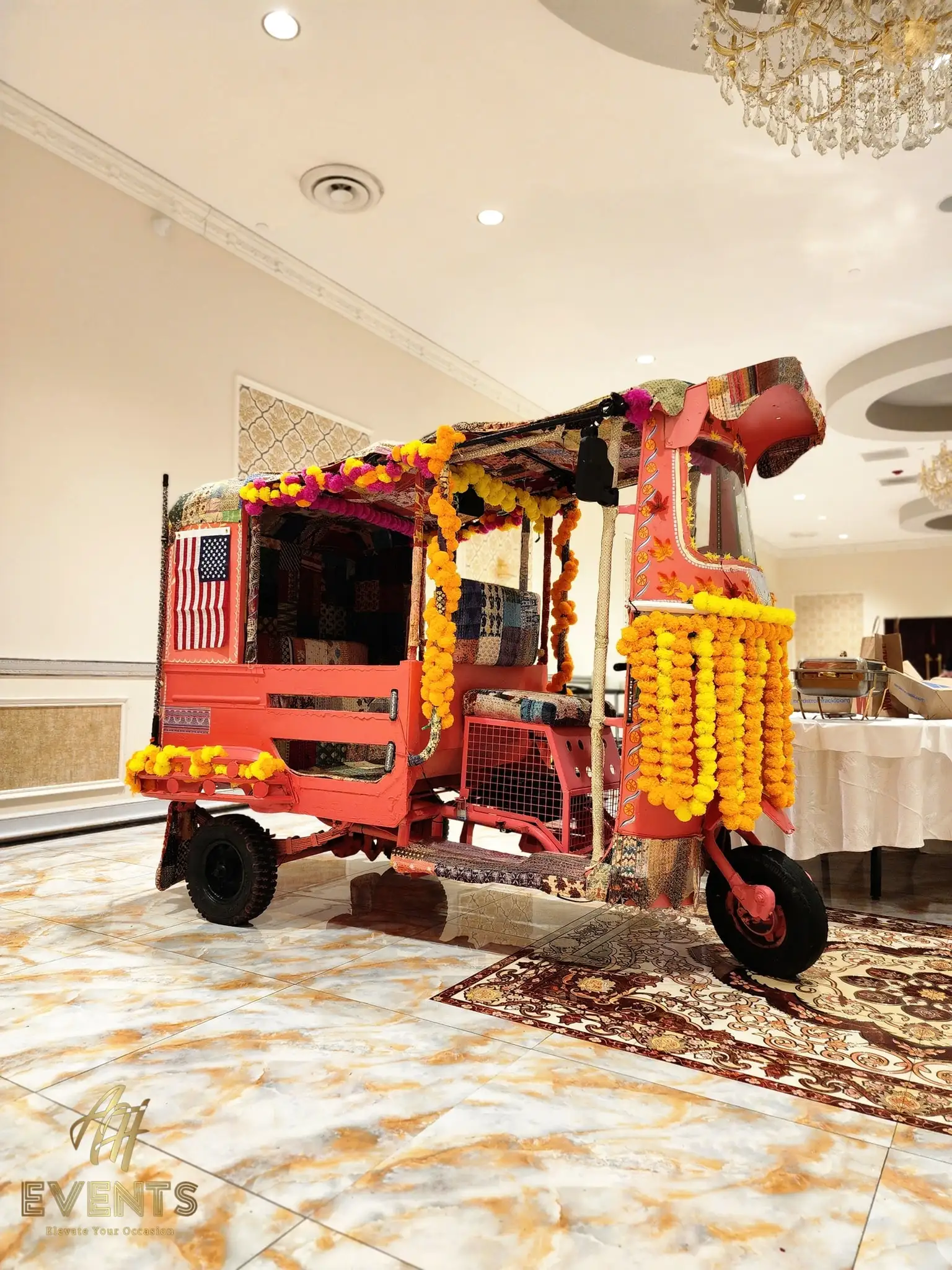 A brightly colored pink and orange auto-rickshaw decorated with yellow marigold garlands and blue LED lights