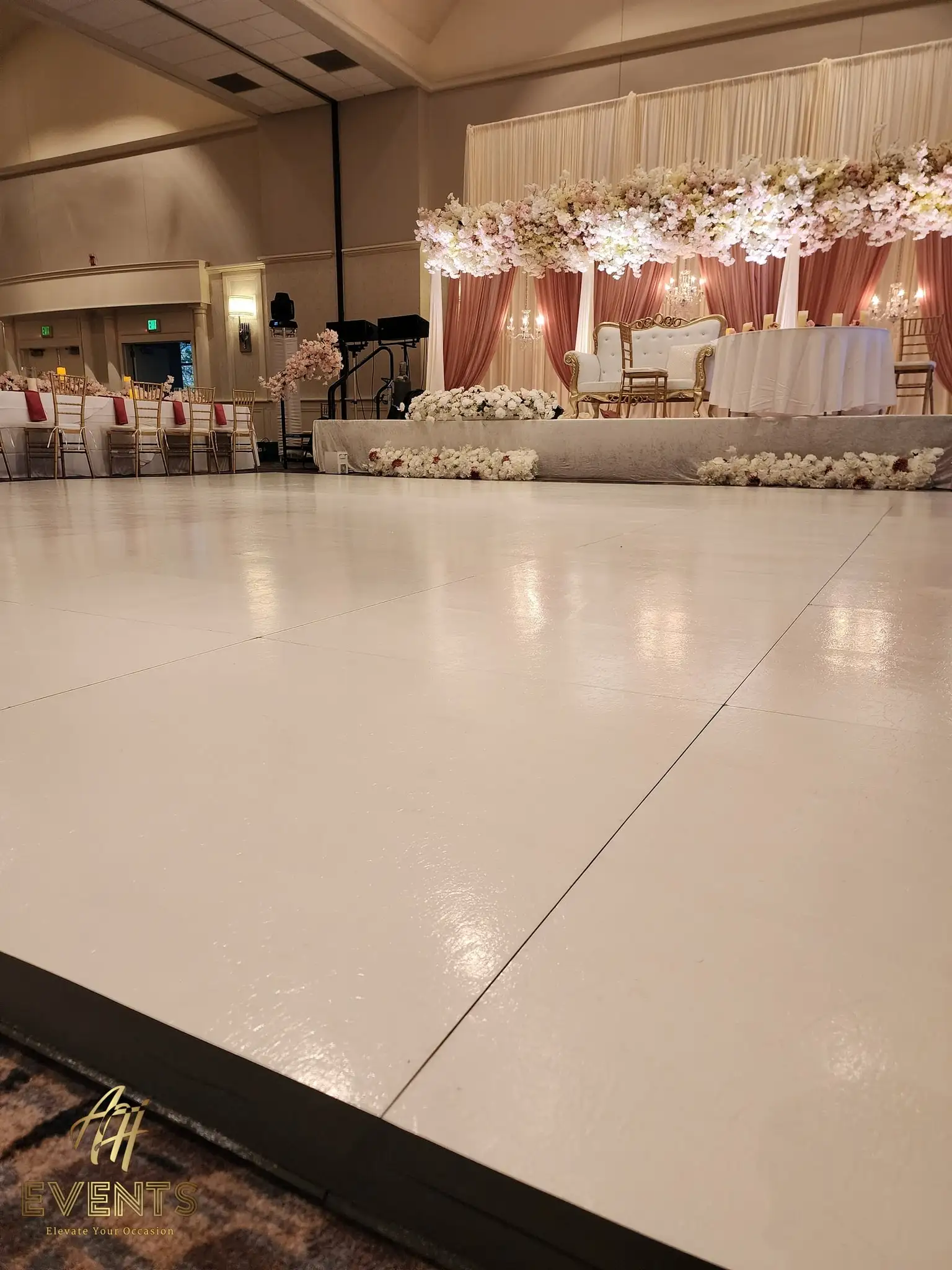 White dance floor leading to a gold loveseat on a blush-canopied floral stage