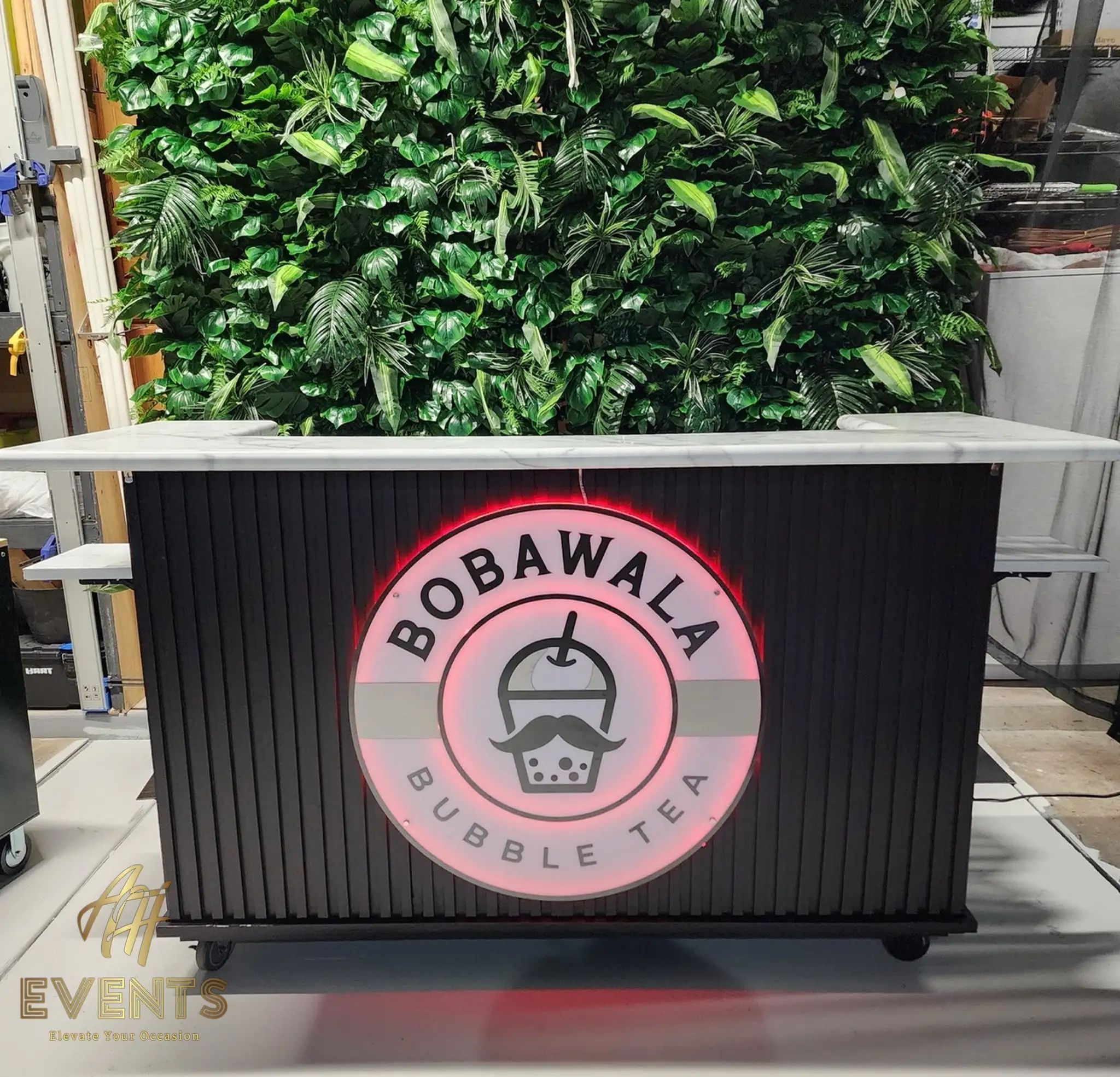 Bobawala cart with its circular logo backlit red against the black slatted front, before a greenery wall