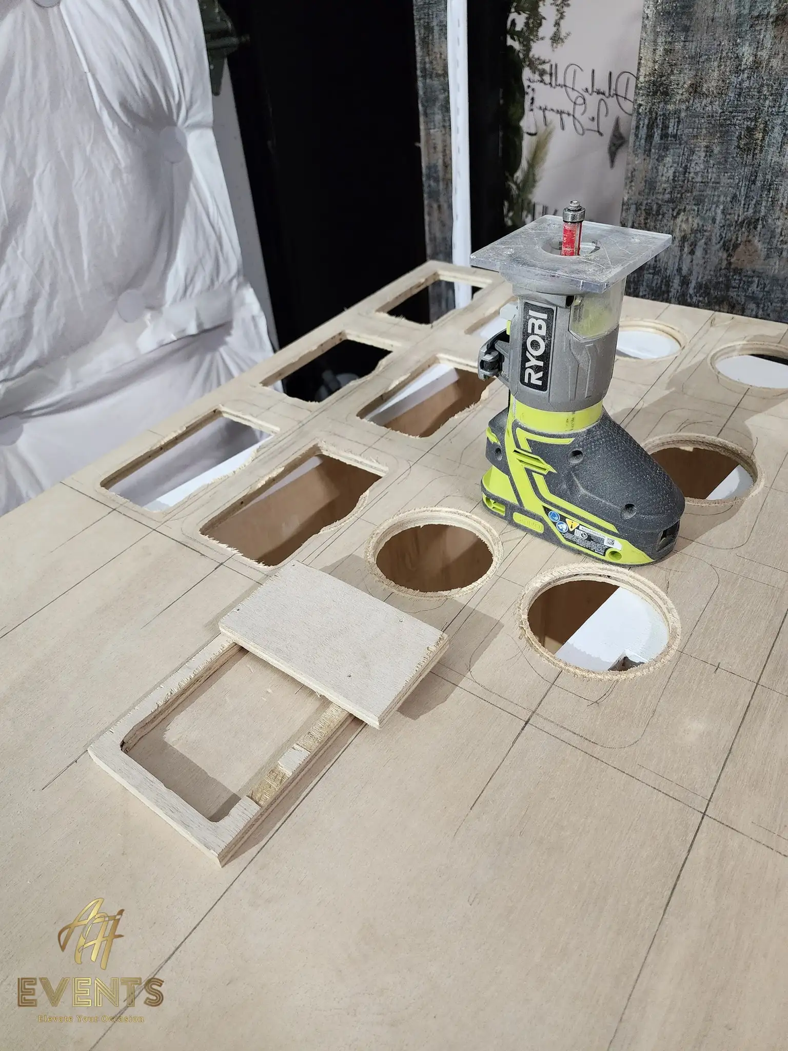 Ryobi trim router sitting on the plywood cart top mid-cut, among rectangular wells and circular cup holes