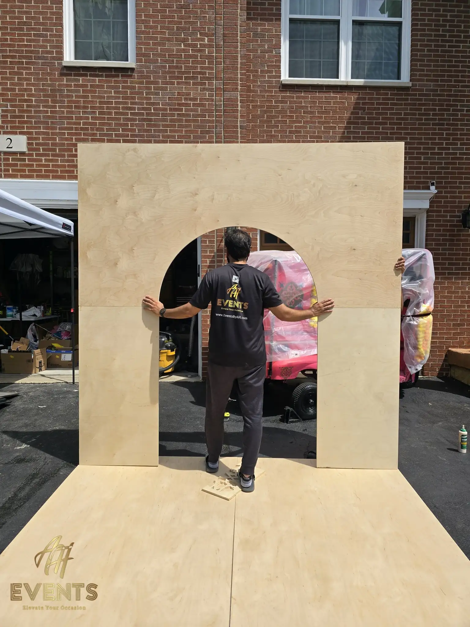 Builder holding the plywood arch backdrop wall upright in the driveway as it is assembled
