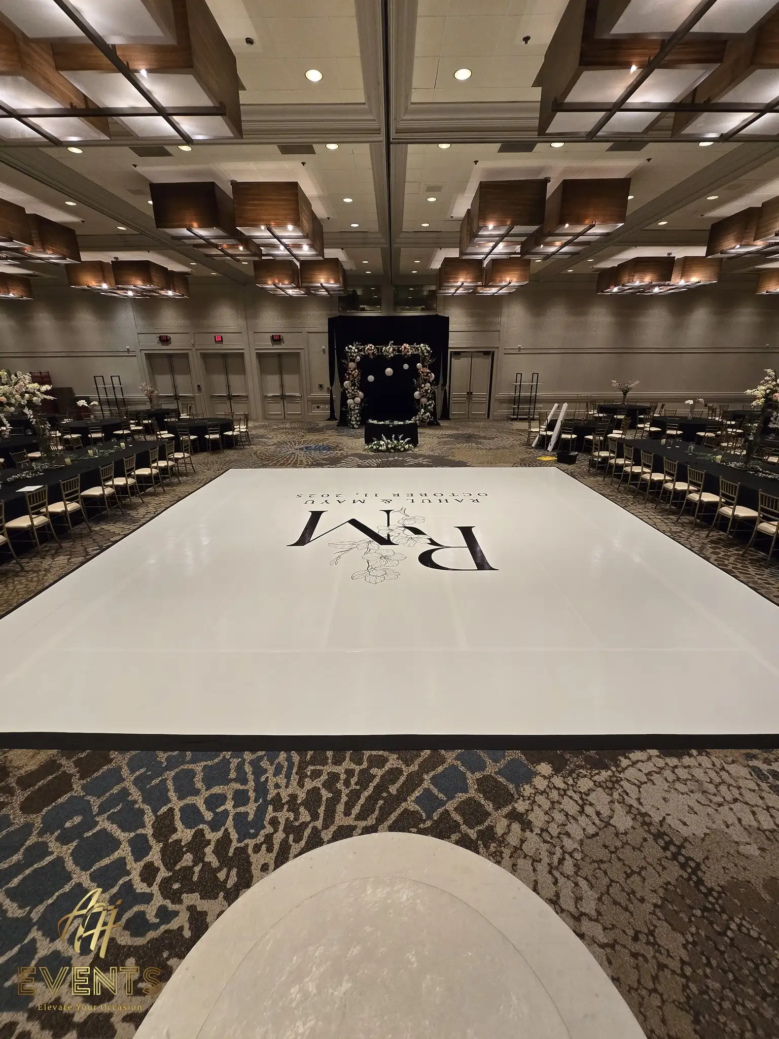 Angled view of the white 'R M' monogram dance floor facing the black floral-backdrop stage