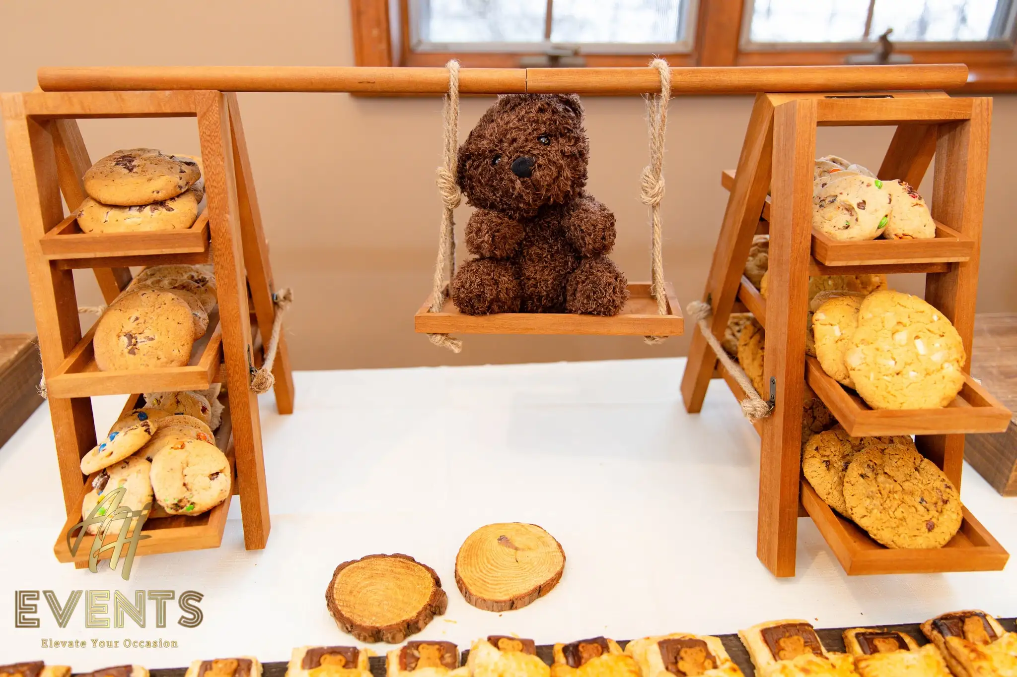 Wooden dessert stand of cookies with a brown teddy bear on a swing and bear-shaped pastries below