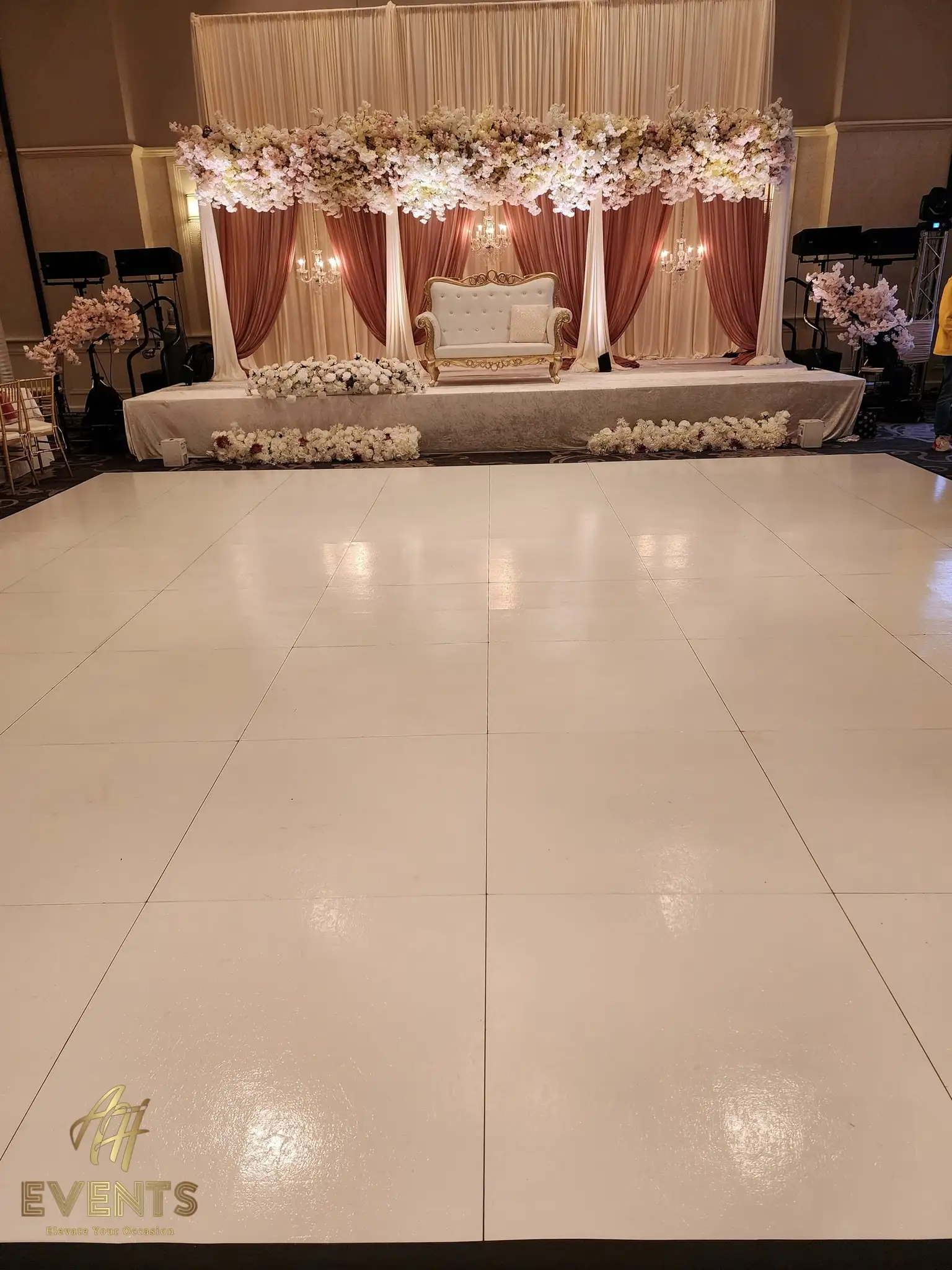 White dance floor in a banquet hall facing a mauve floral stage flanked by cherry-blossom trees