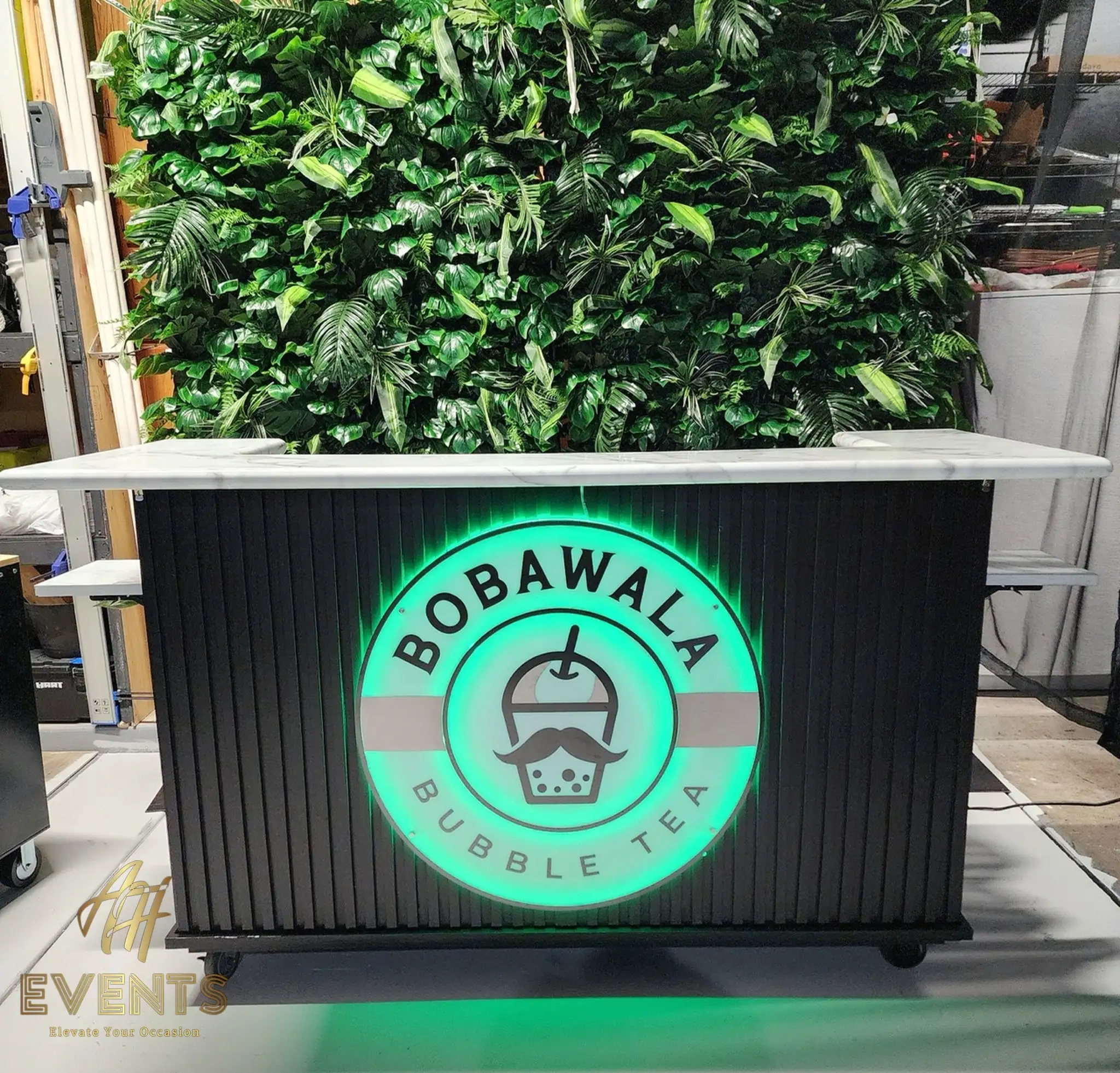 Bobawala cart with the circular logo glowing green on the black slatted front, before a greenery wall