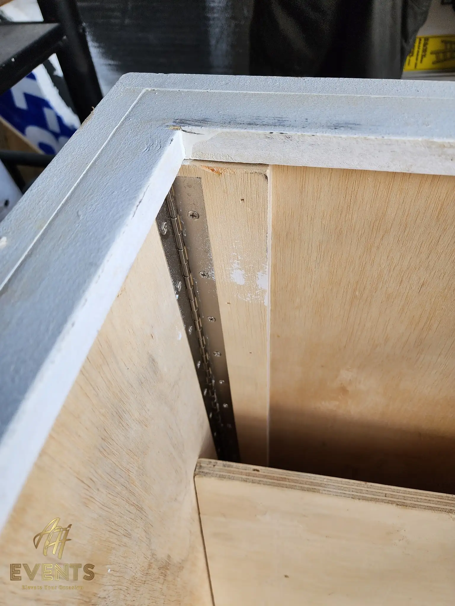Corner joinery detail of the cart box showing a piano hinge and a painted gray frame edge over raw plywood