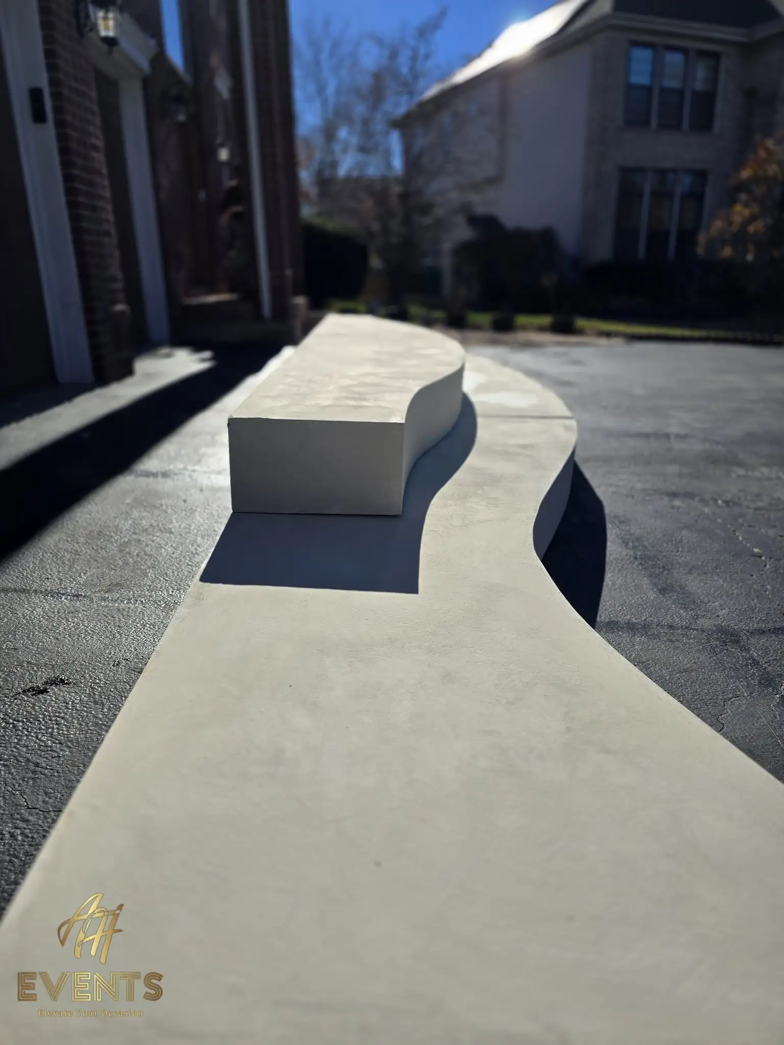 S-curved white stage riser running along the driveway in sunlight, a step block set on top