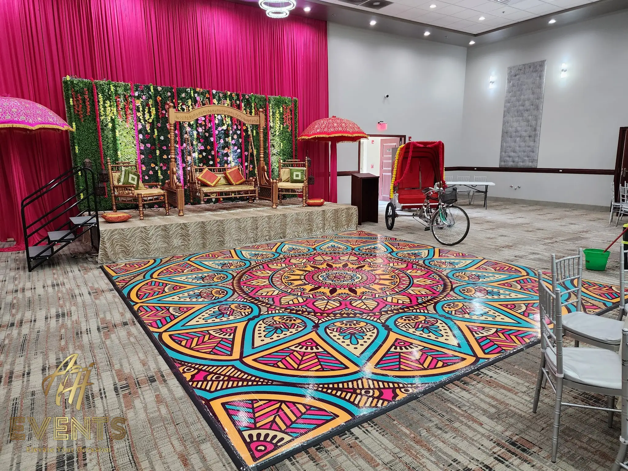 Mandala floor in front of a magenta drape and greenery backdrop with a wooden swing