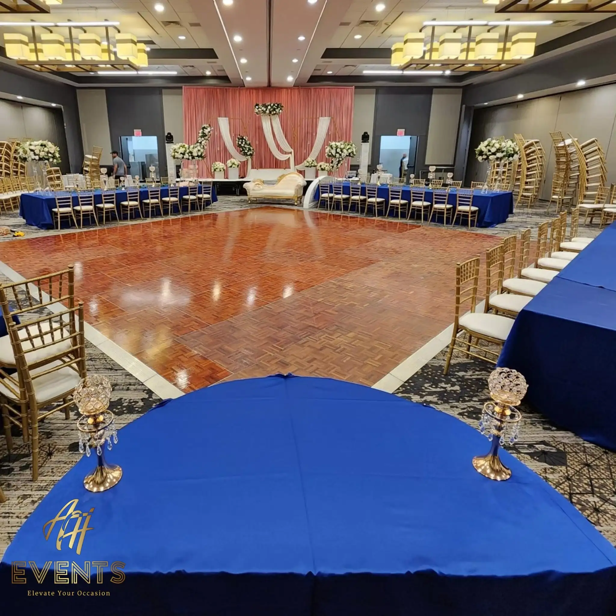 Parquet wood dance floor with a blush stage and gold sofa, royal-blue tables around